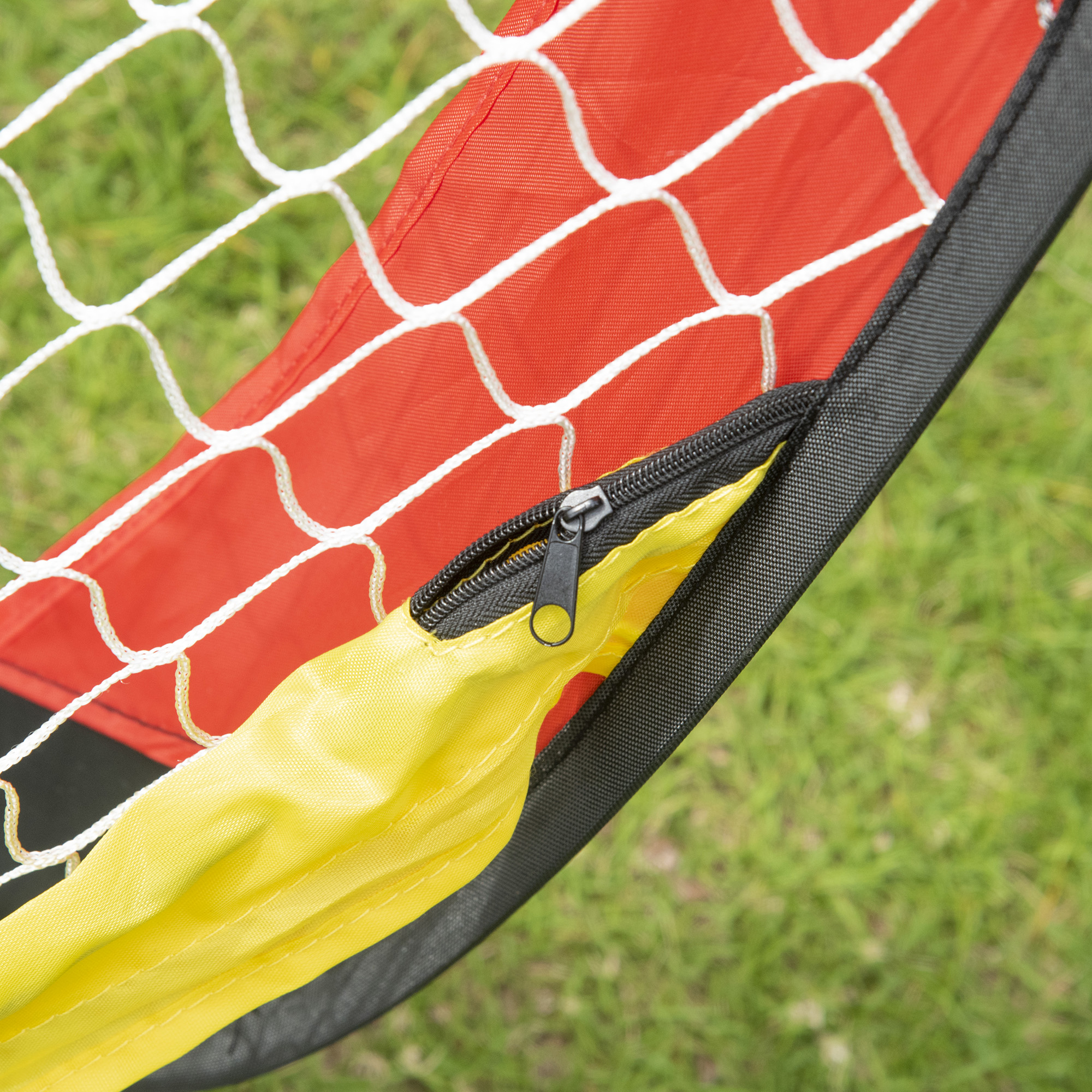 Nahaufnahme eines rot-weißen Fußballnetzes mit gelbem Reißverschluss. Grünes Gras im Hintergrund.