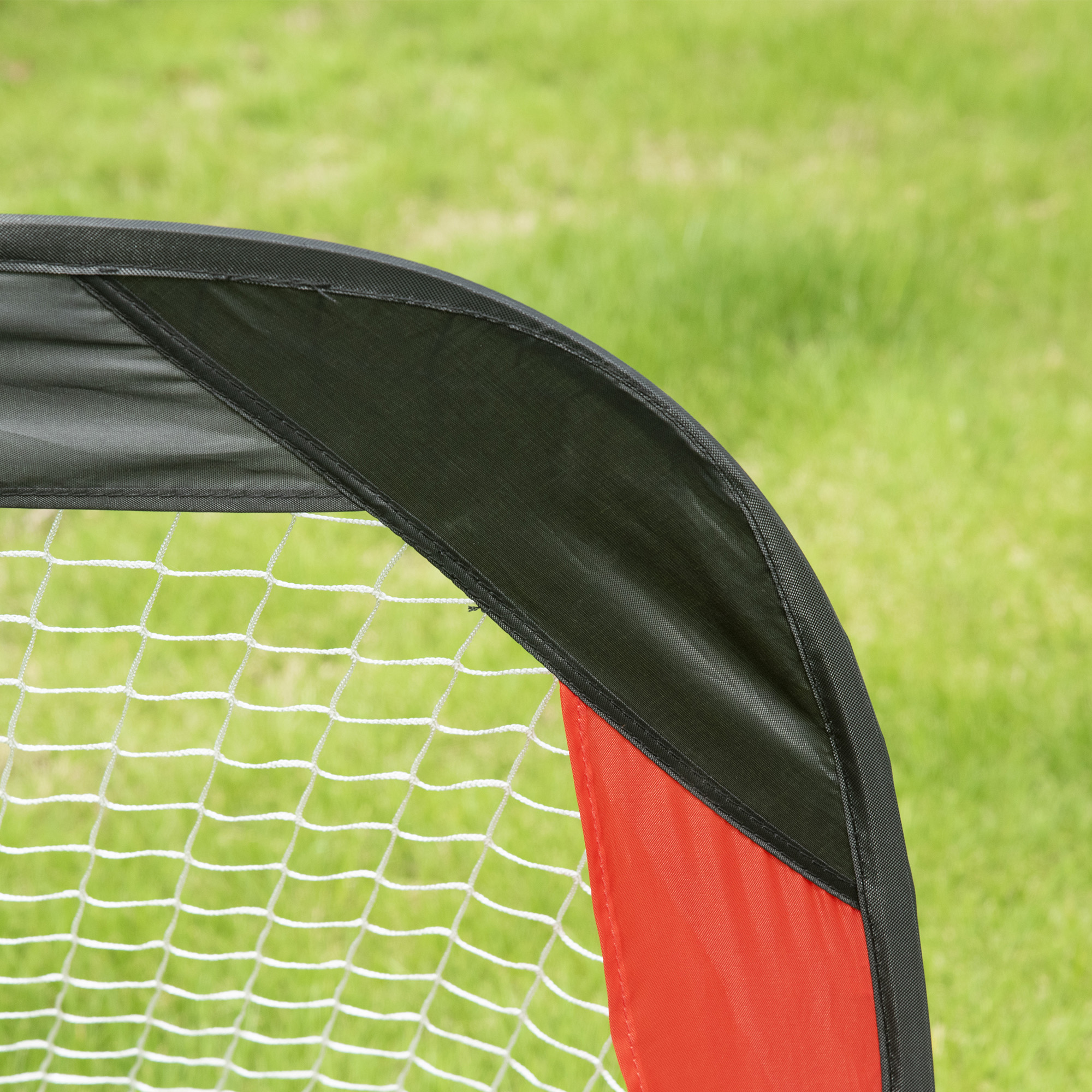 Nahaufnahme eines roten und schwarzen Fußballtornetzes. Grüner Gras Hintergrund. Das Netz ist weiß.