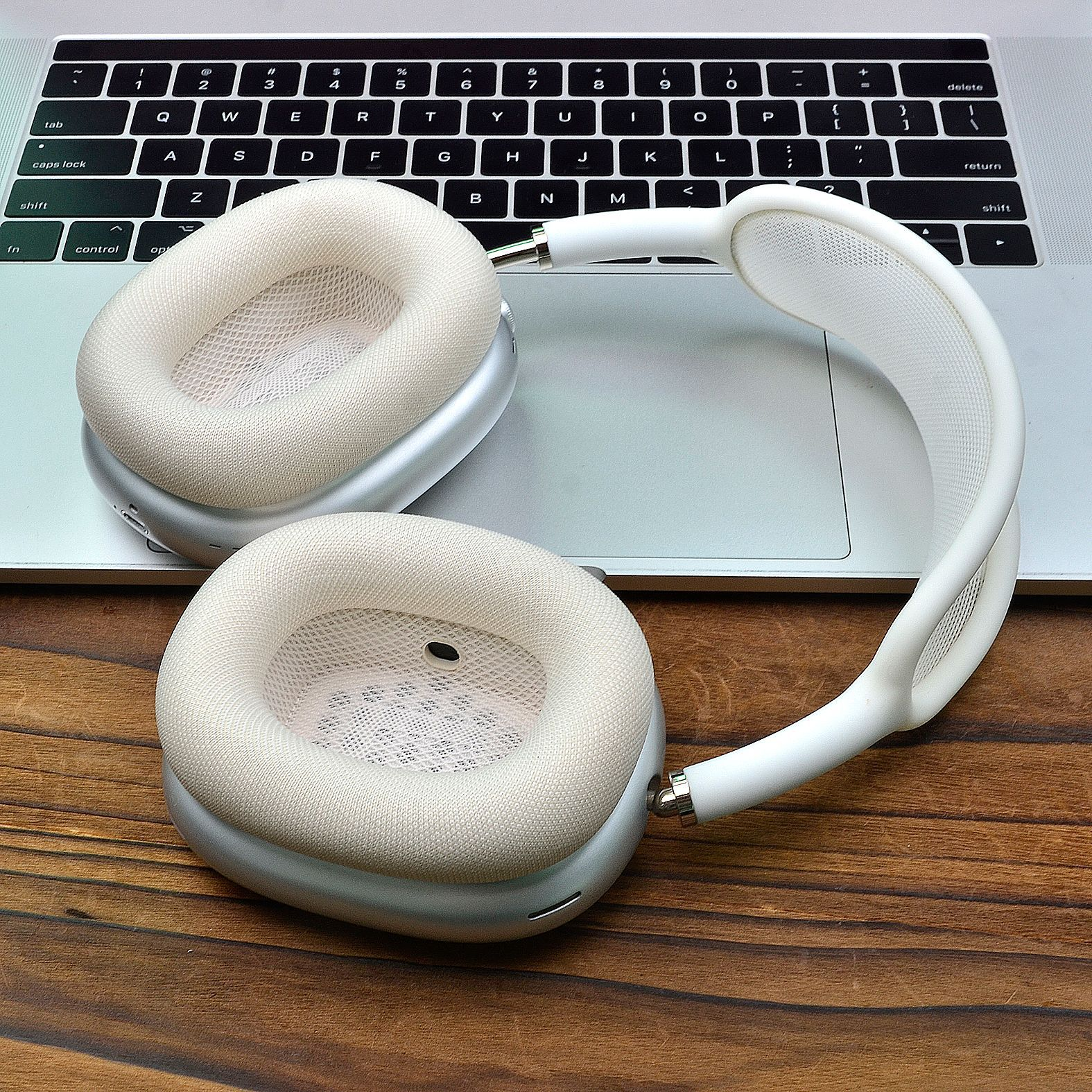 Cuffie bianche con accenti argentati, appoggiate su un laptop su una scrivania in legno.