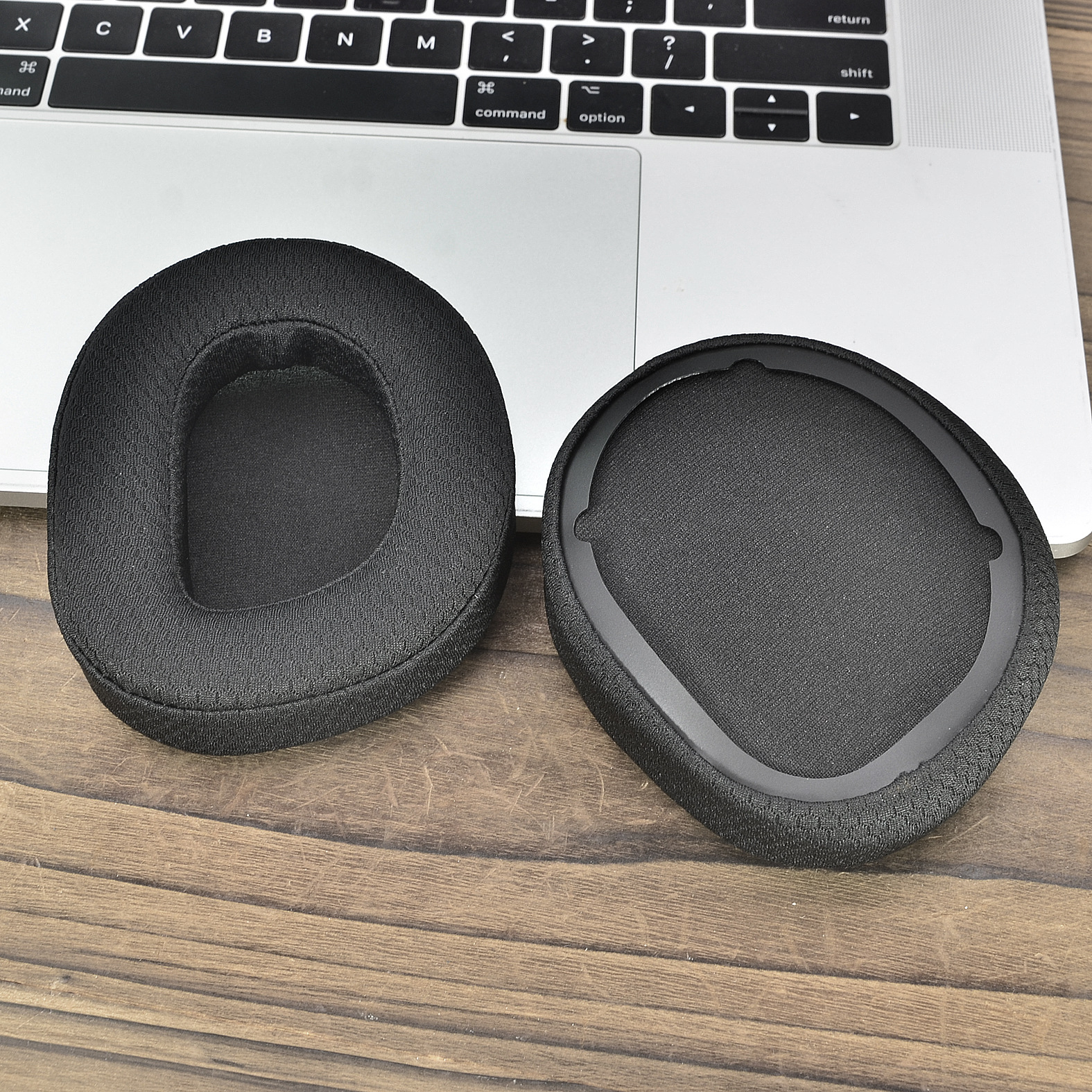 Due padiglioni neri per cuffie, uno su una tastiera di un laptop, l'altro su superficie in legno.
