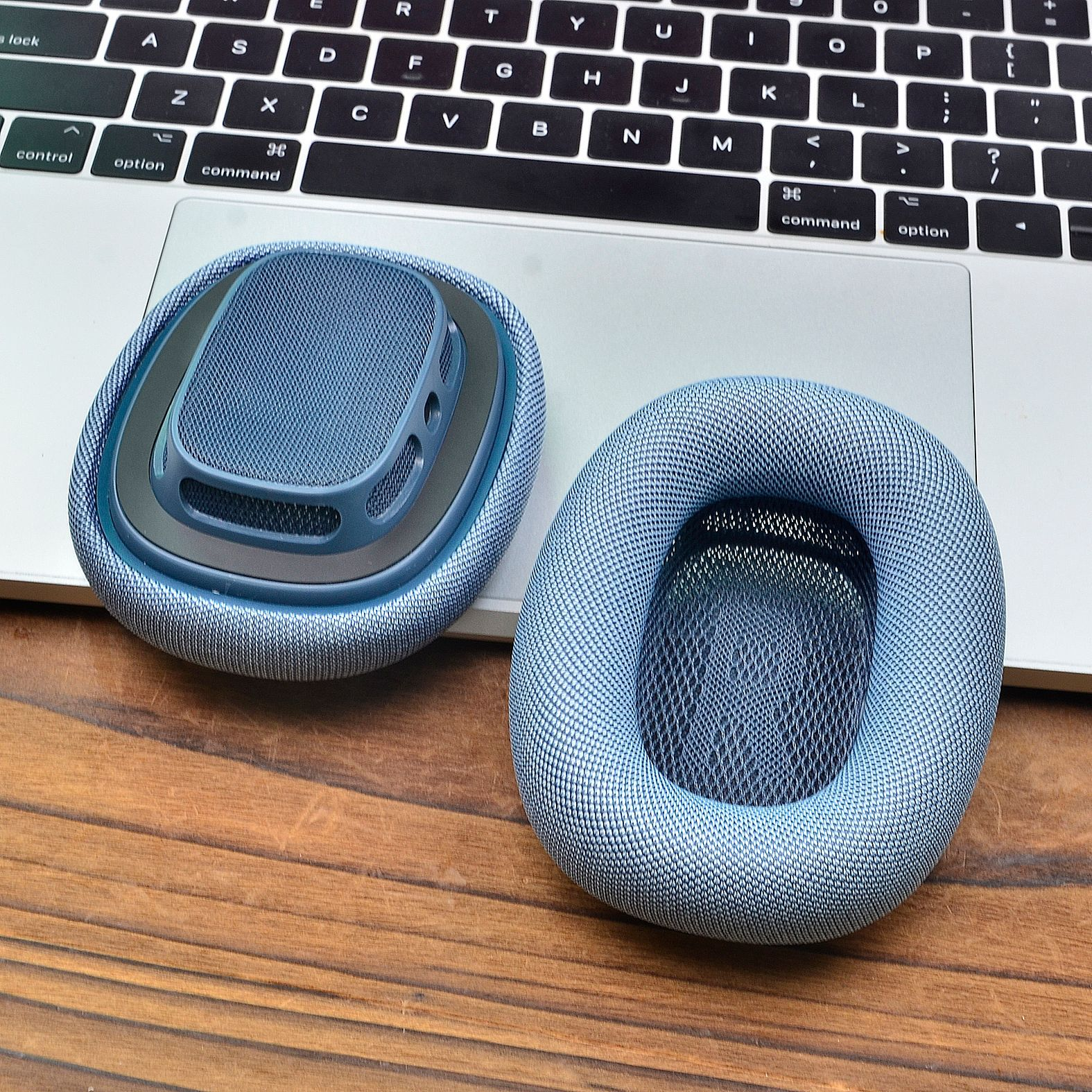 Zwei blaue Kopfhörer, einer davon geöffnet, auf einem Laptop. Die Kopfhörer liegen auf einem Holztisch.