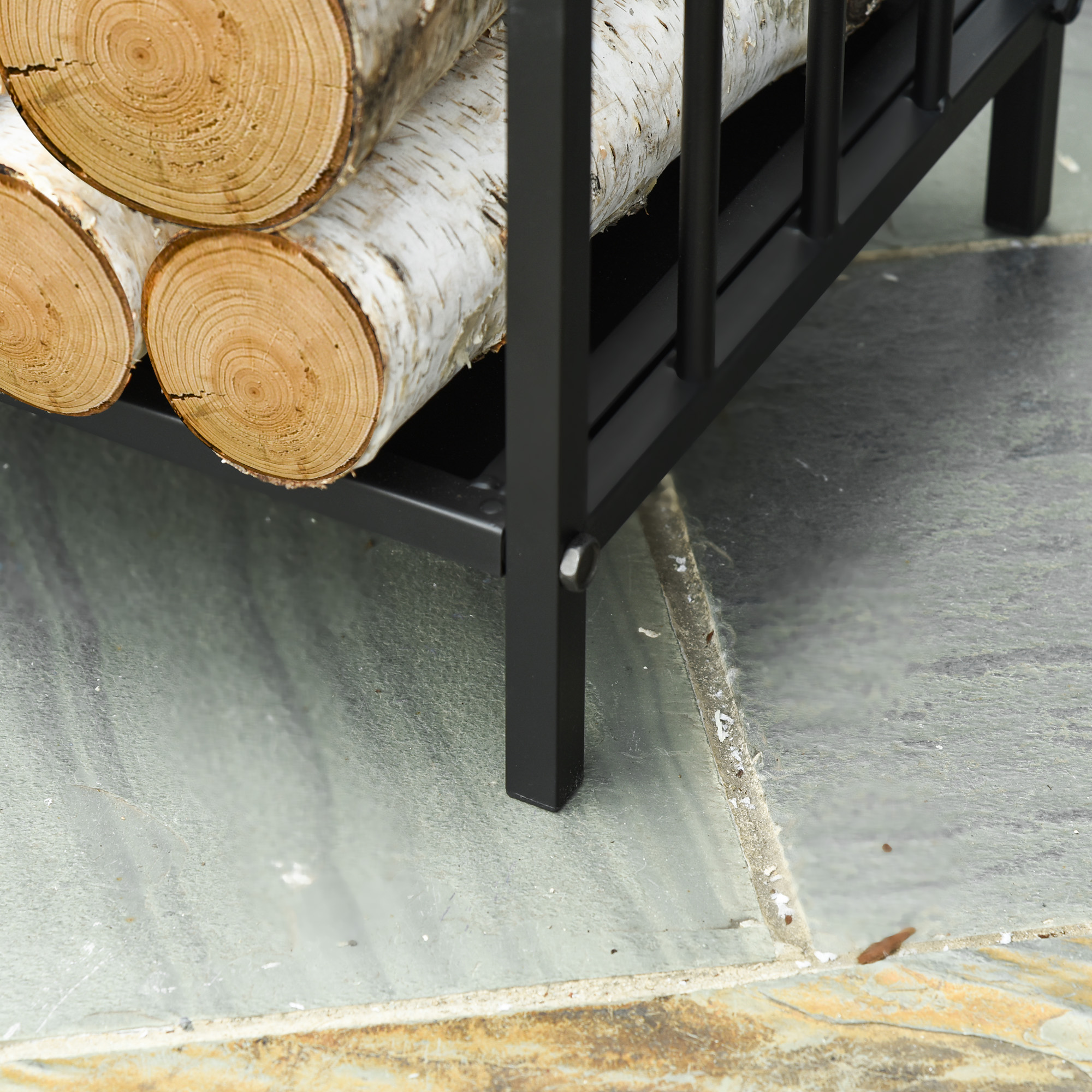 Nahaufnahme eines schwarzen Metall-Holzhalters mit Birkenstämmen auf Steinplatten.