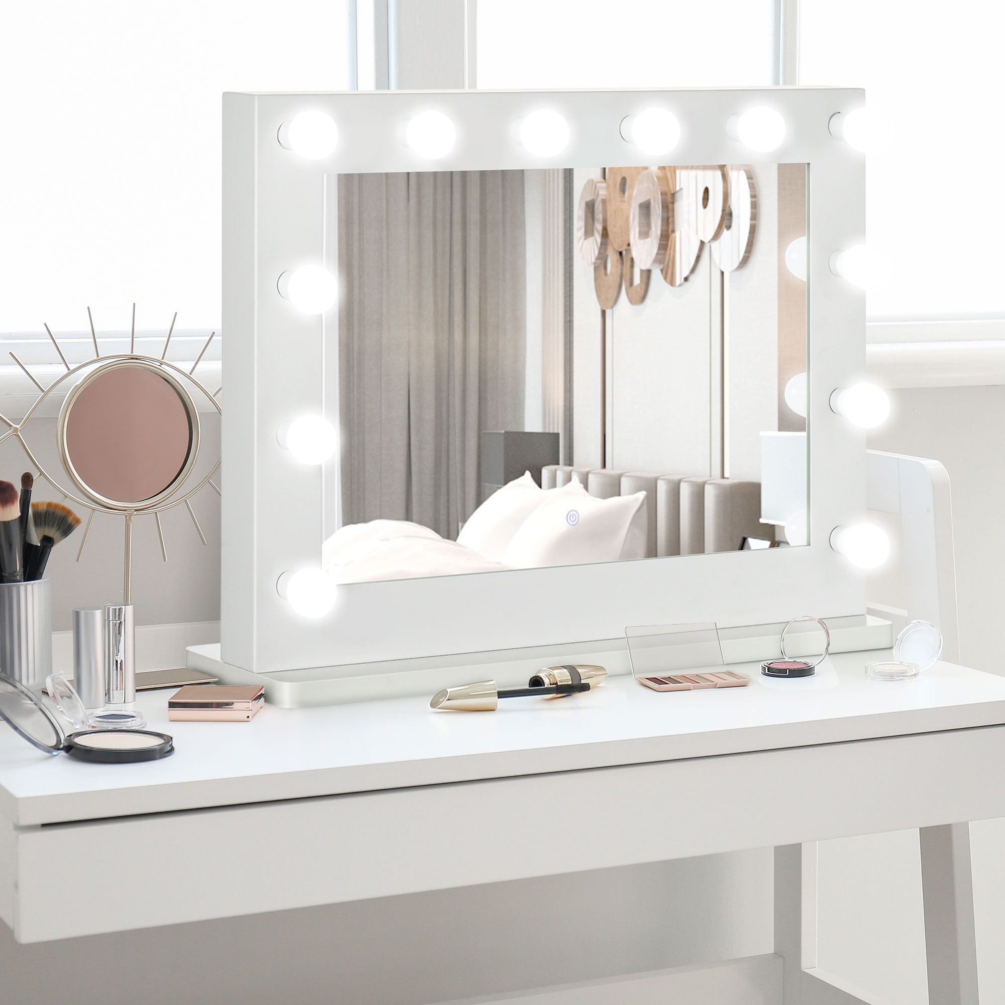 Schminktisch mit Spiegel und Lichtern, Make-up-Artikeln und einem Pinselset auf einem weißen Tisch.