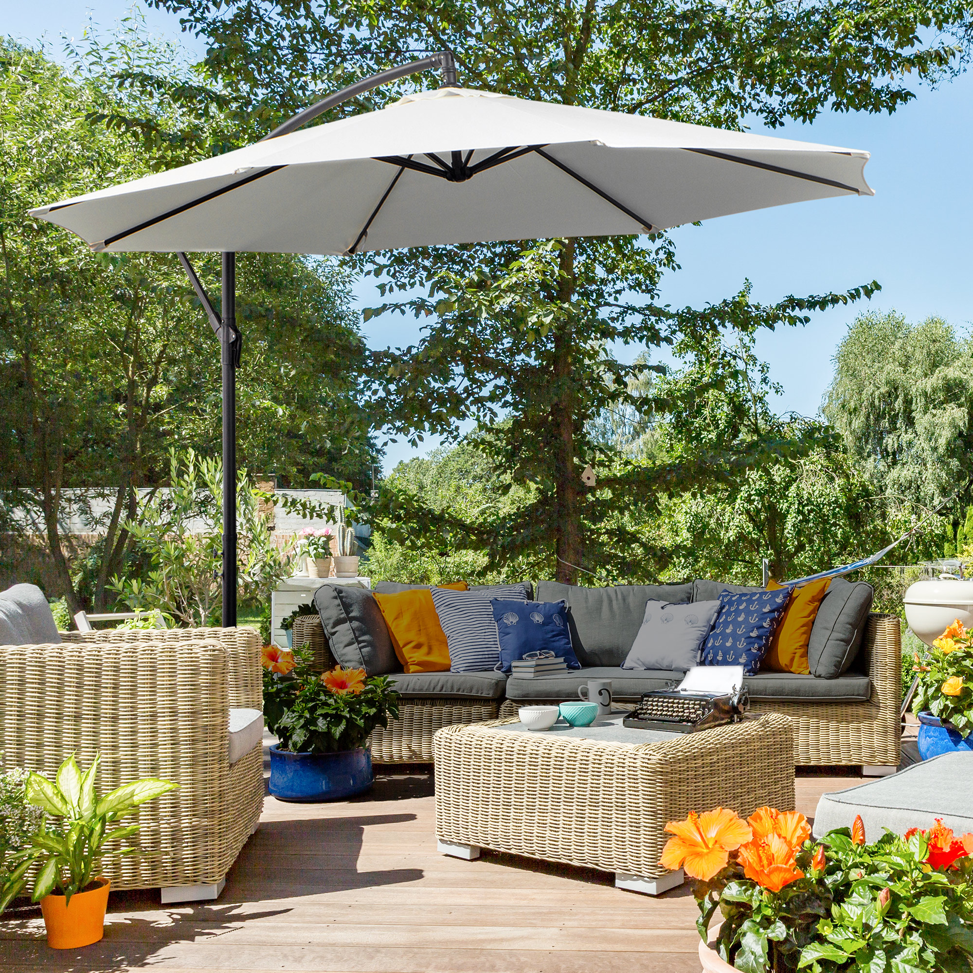 Szene auf der Terrasse mit weißem Sonnenschirm, Sitzbereich und grünem Laub.