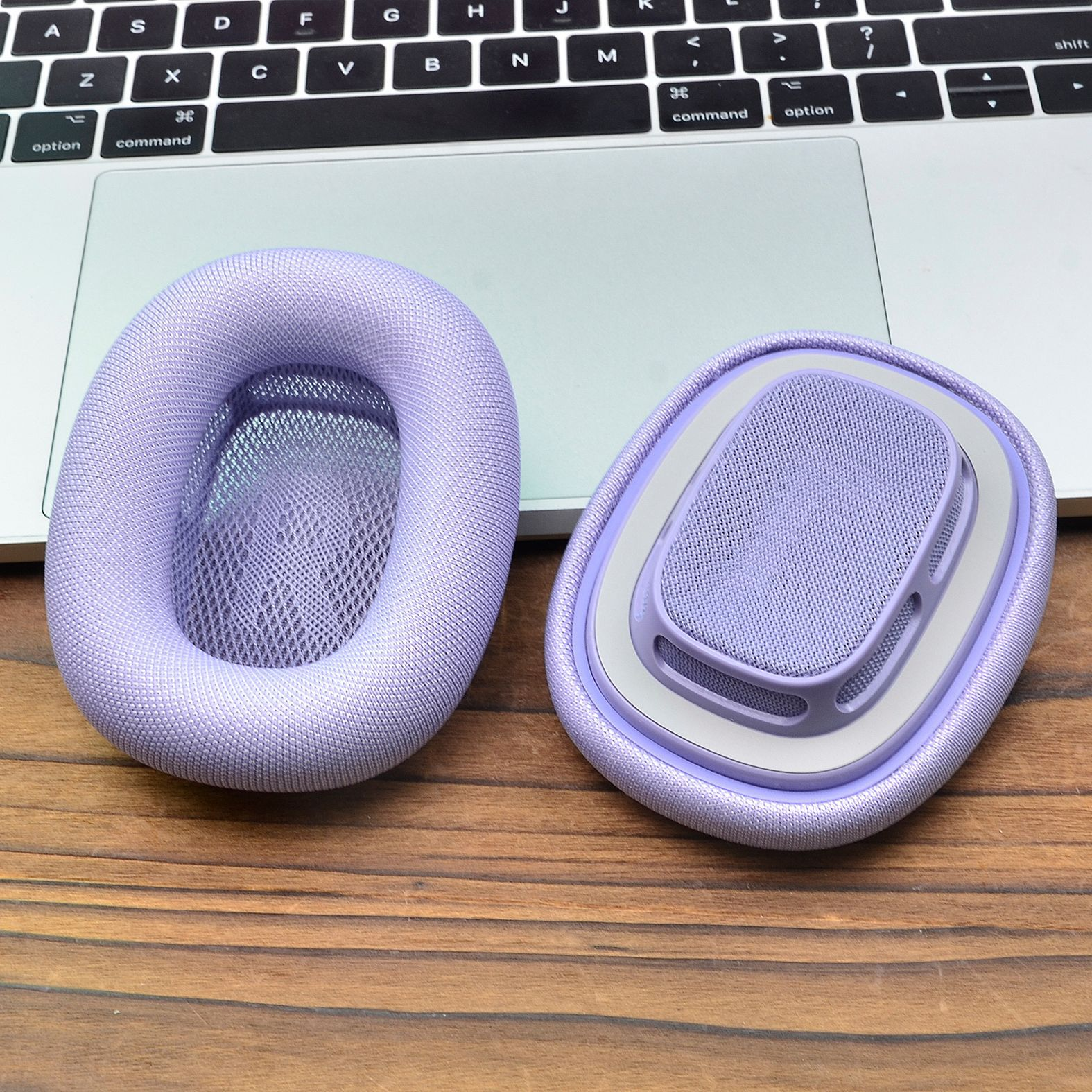 Coppia di cuscinetti auricolari viola accanto a una tastiera di un laptop. Superficie in legno.