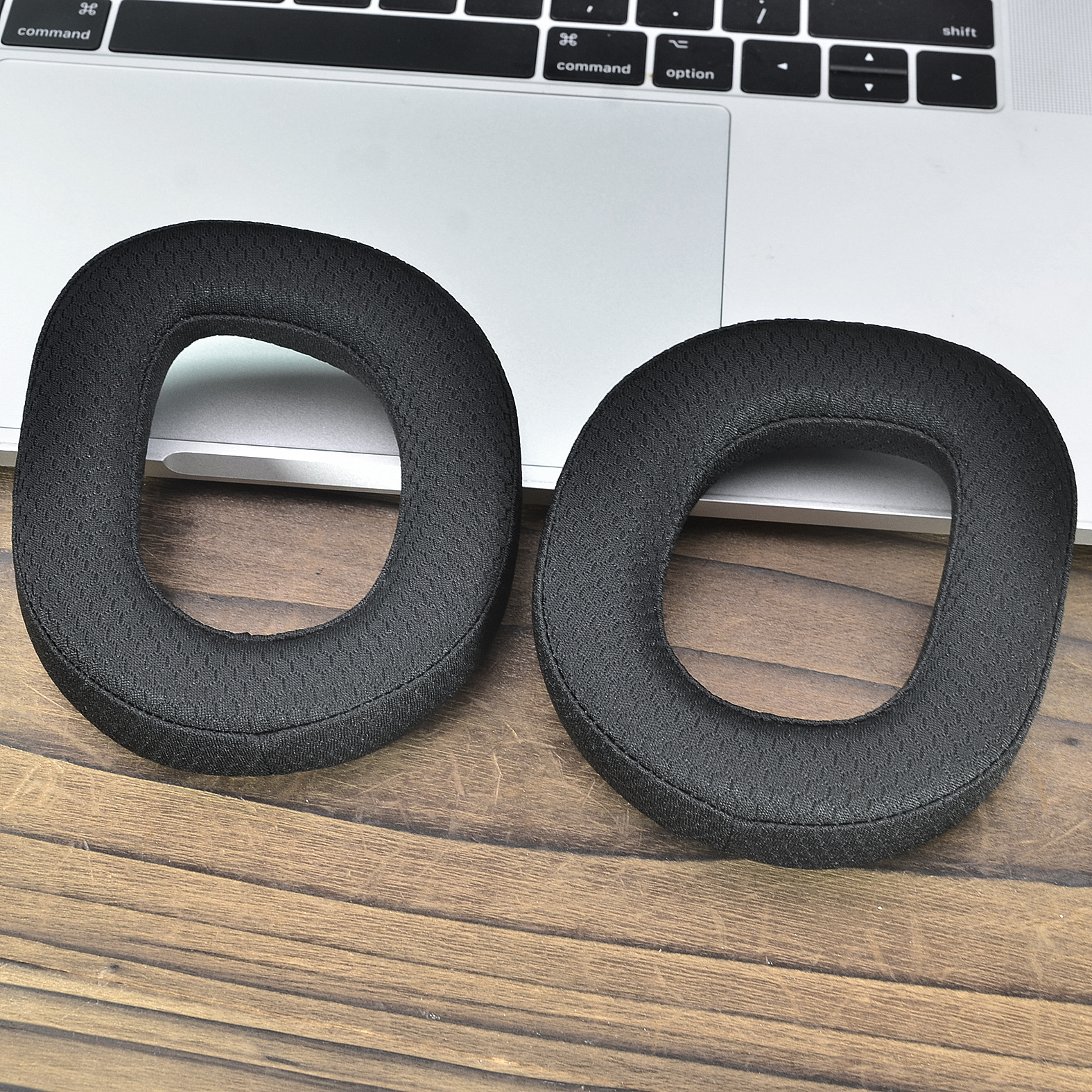 Due cuscinetti auricolari neri circolari su tavolo di legno, vicino a laptop argentato.
