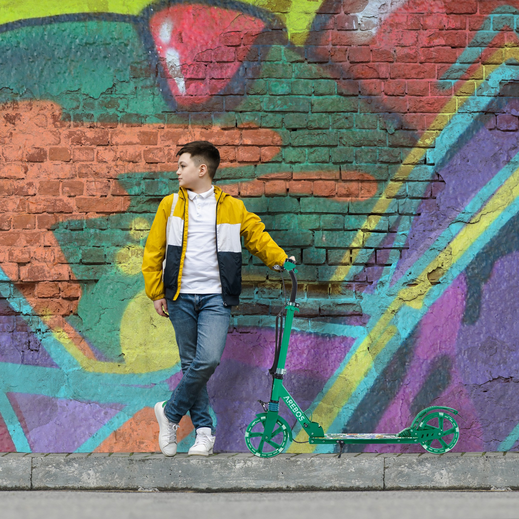 Teenager mit einem grünen Roller, der sich an eine Wand mit Graffiti lehnt.
