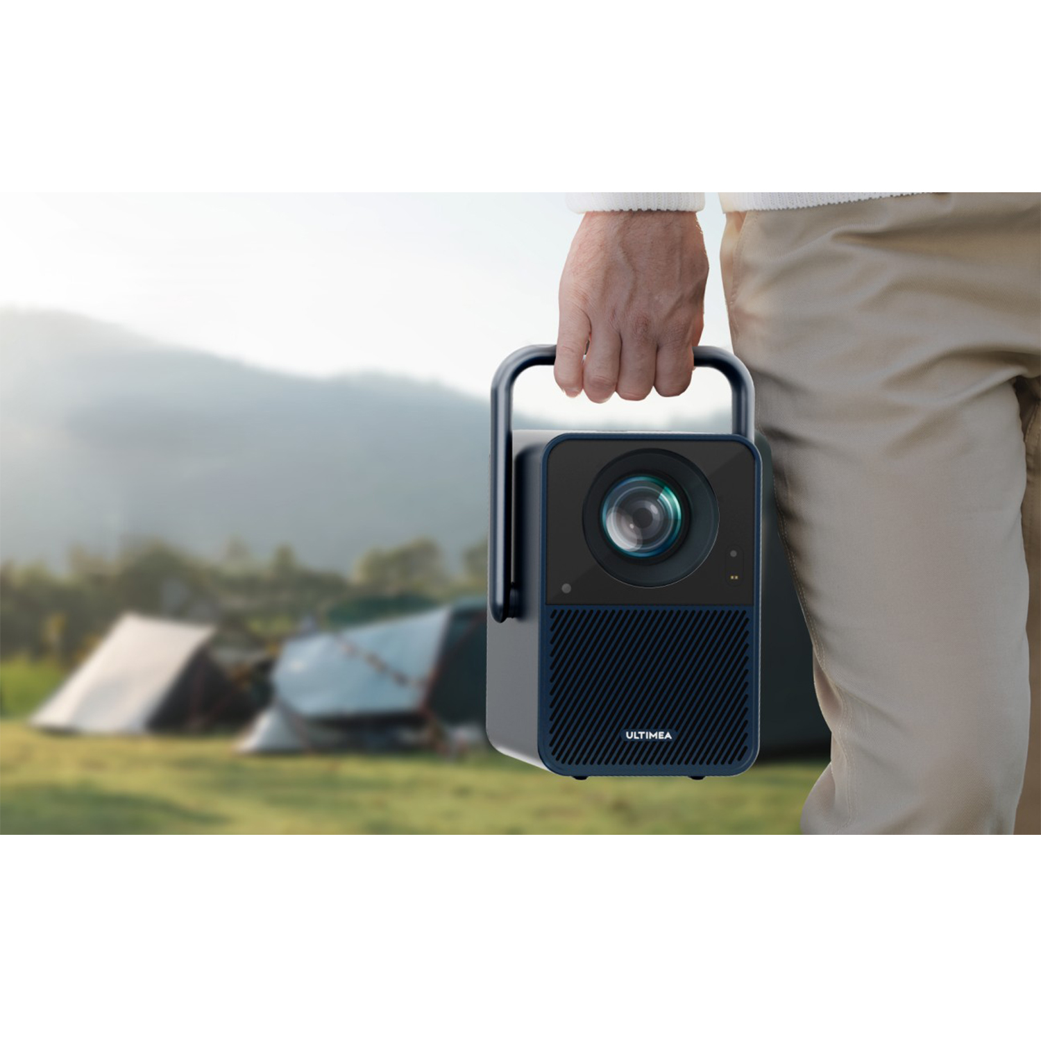 Osoba trzymająca projektor w dłoni, niebieski i czarny. Tło namiotu i góry.