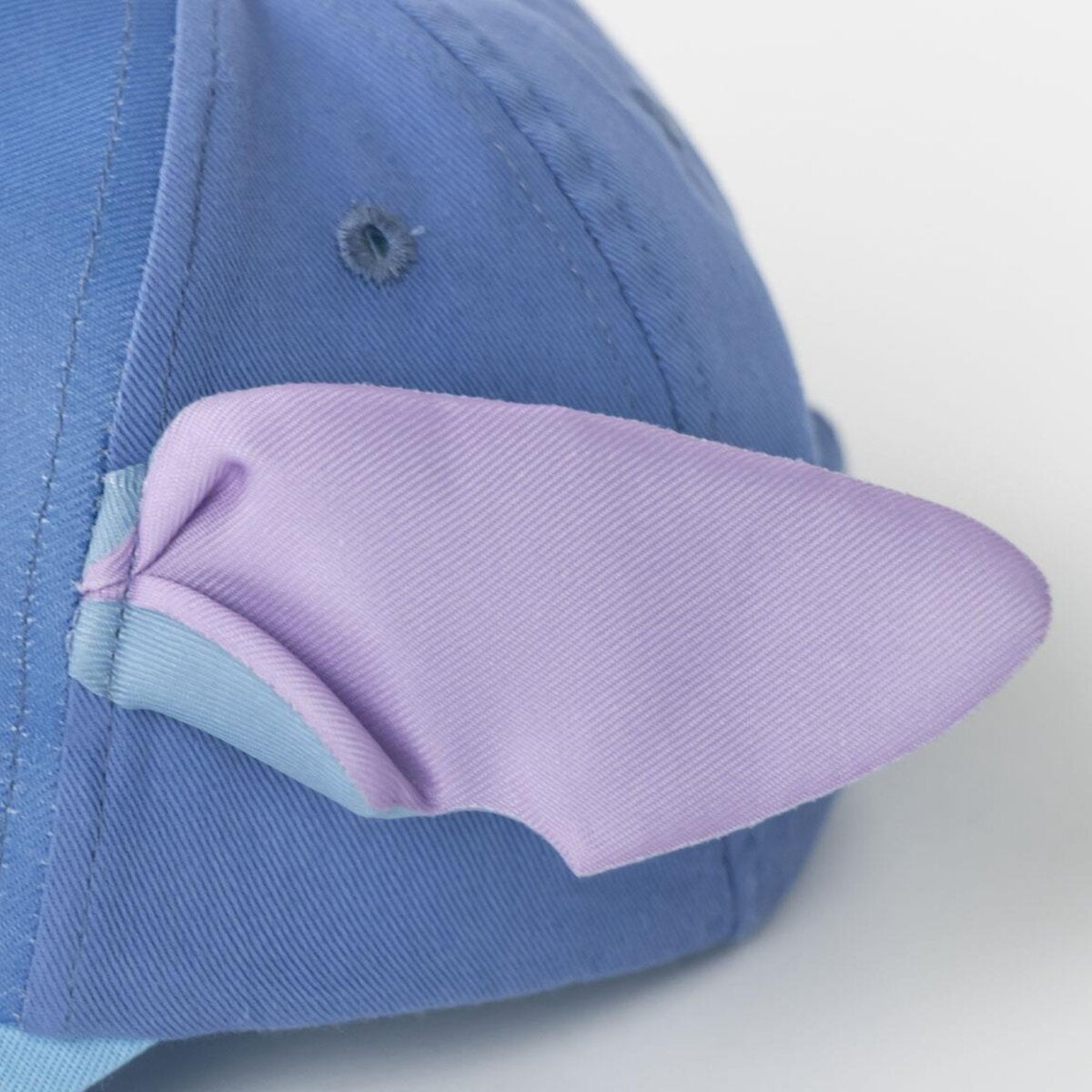 Primer plano de una gorra de béisbol azul de Stitch con un detalle de oreja morada. Fondo blanco.