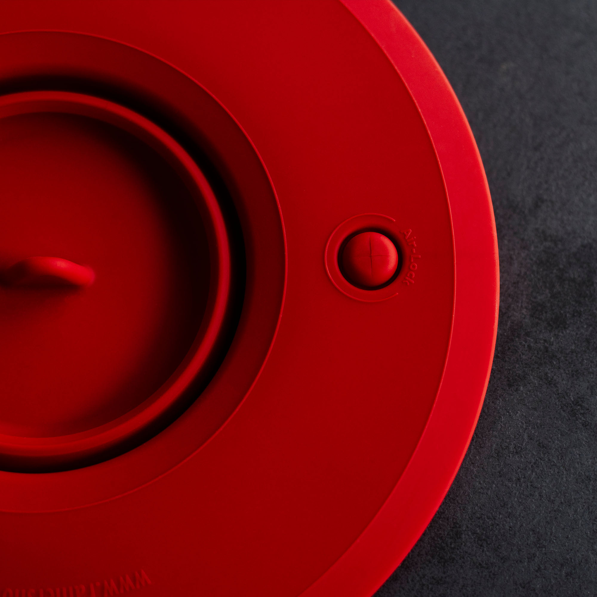 Roter Deckel mit Knopf und Knopf auf dunkler Oberfläche. Der Deckel hat ein kreisförmiges Design.