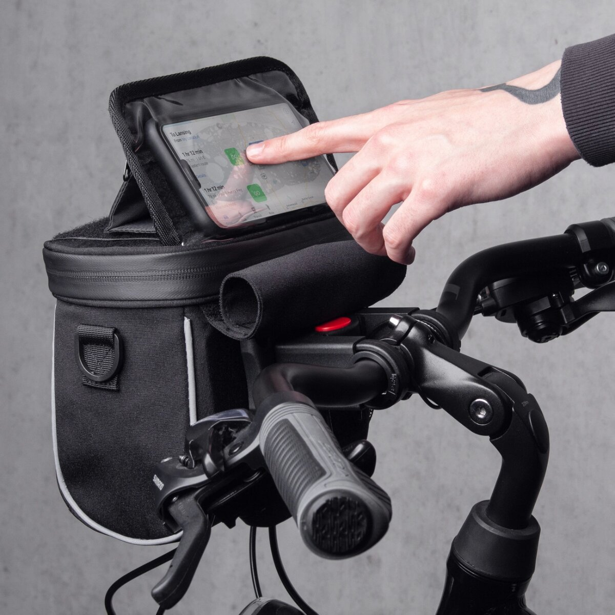 Die Hand einer Person berührt ein Telefon in einer Fahrradlenkertasche.