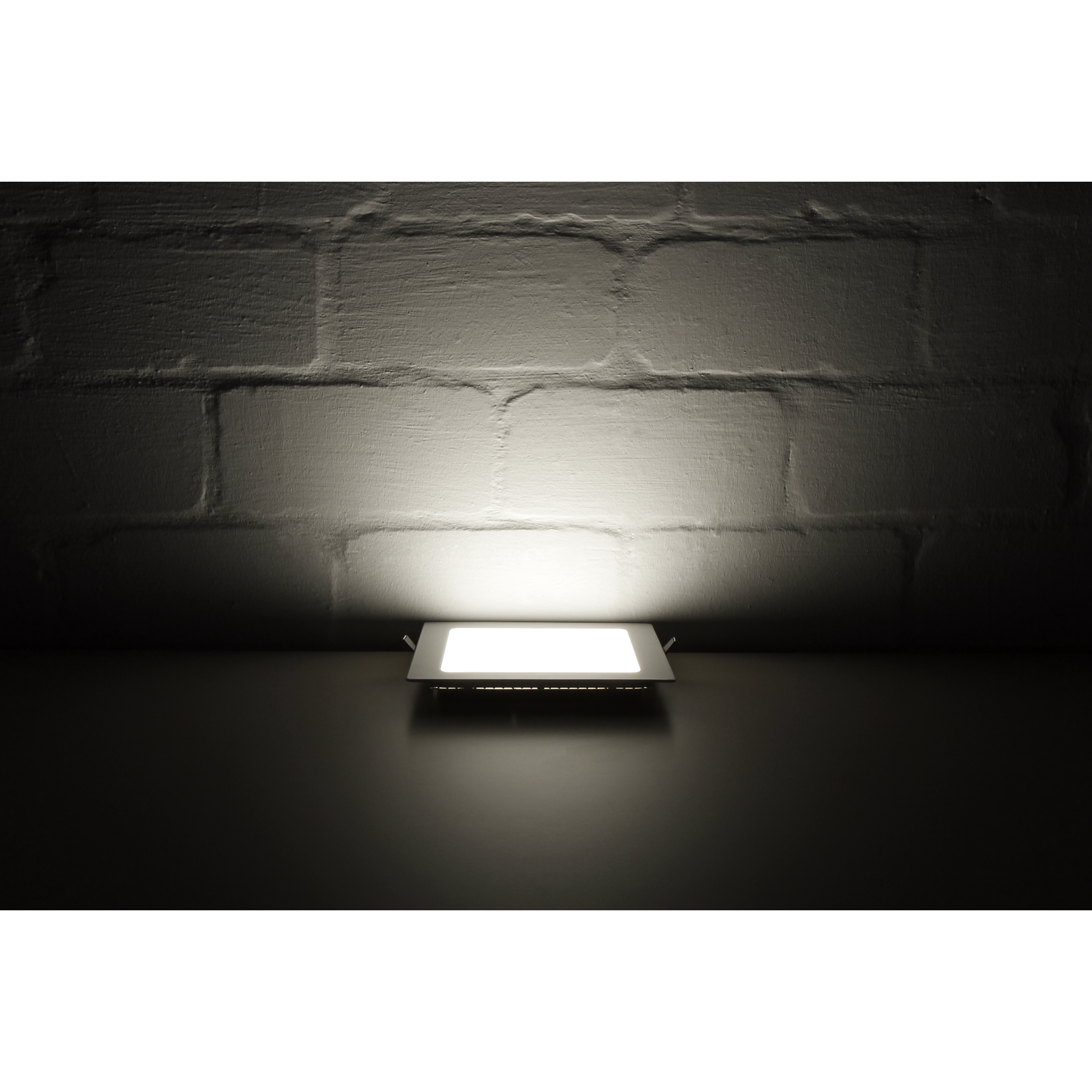 Ein eingelassener quadratischer LED-Scheinwerfer, der hell auf eine weiße Backsteinmauer scheint, in dunkler Umgebung.