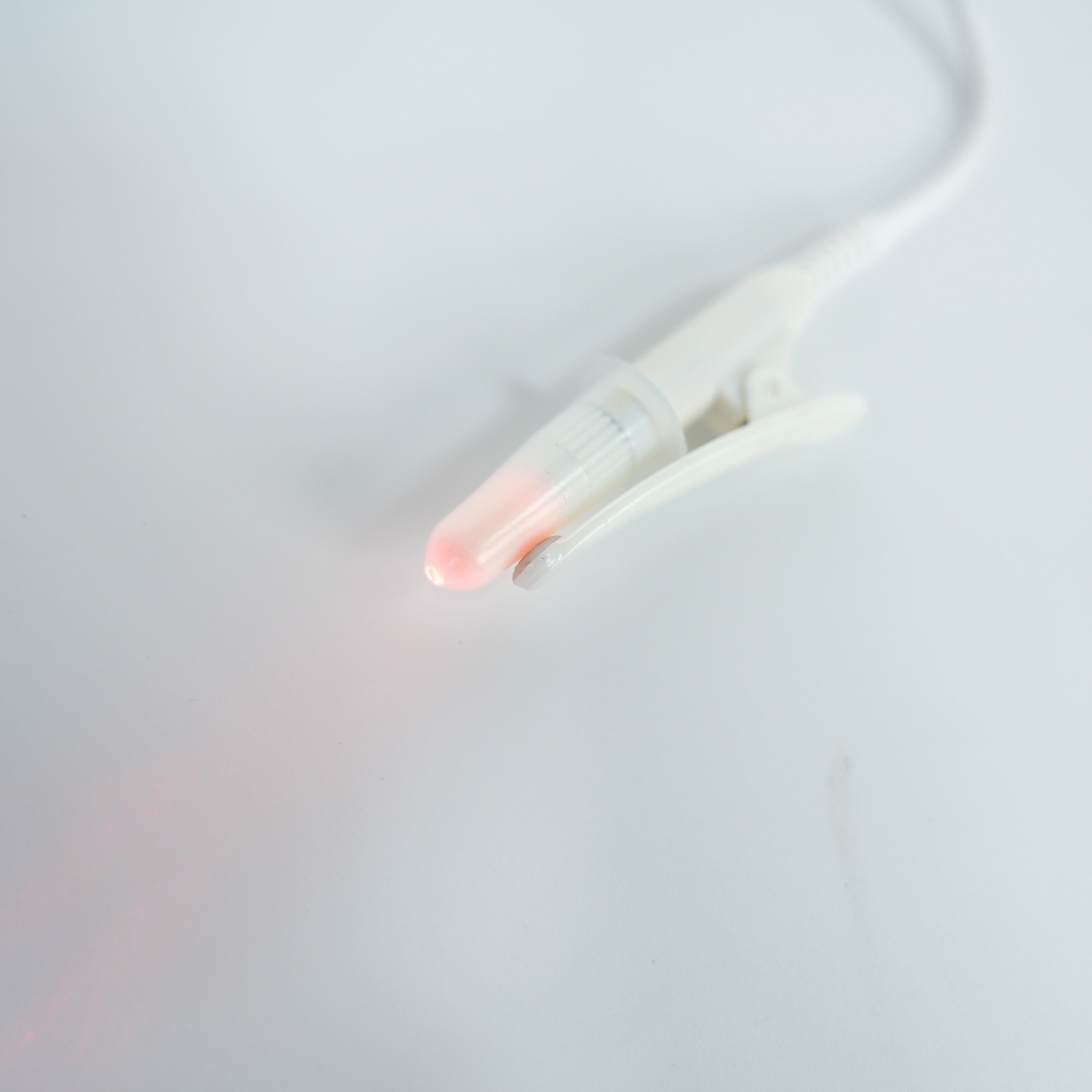 Ein weißes medizinisches Gerät mit rotem Licht, das von der Spitze scheint, auf weißem Hintergrund.