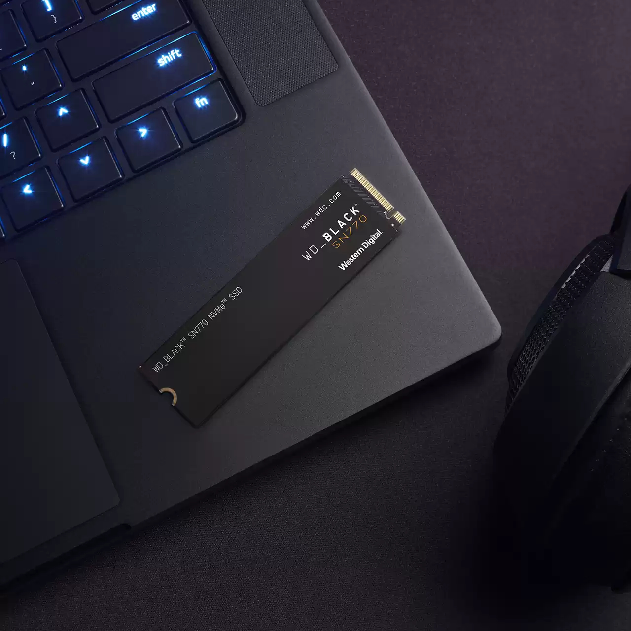 Laptop nero, SSD nero sul touchpad. L'SSD legge WD BLACK SN770. Cuffie nelle vicinanze.