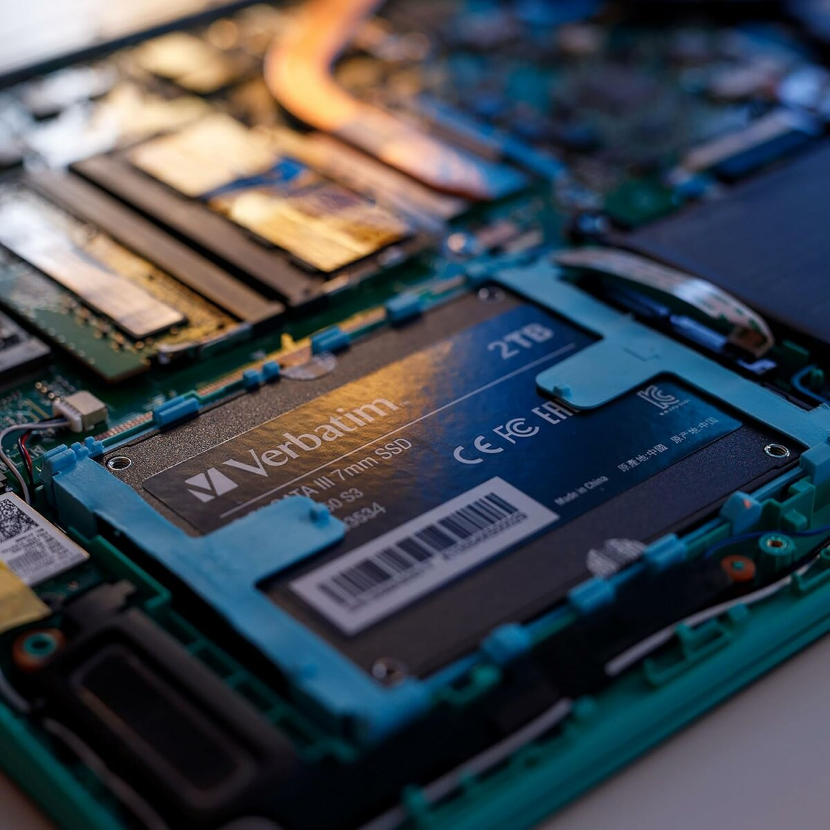 Wewnątrz laptopa widać dysk SSD Verbatim 2 TB. Dysk SSD jest w niebieskiej ramce. Widoczne są różne komponenty.