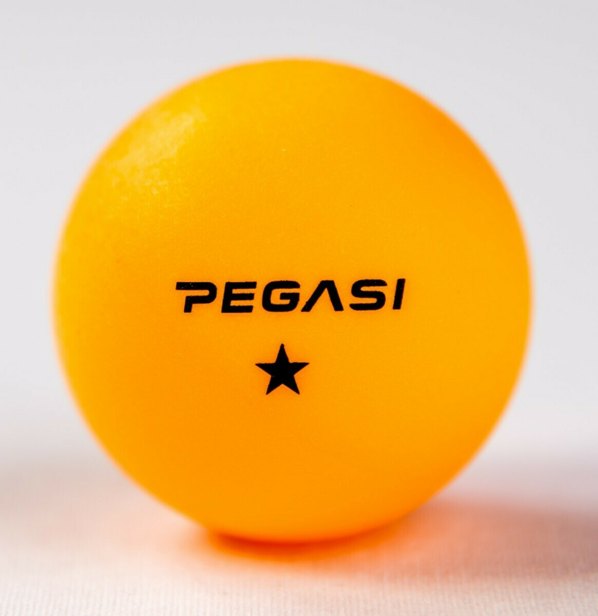 A bright orange ping pong ball with the word 'PEGASI' and a black star.