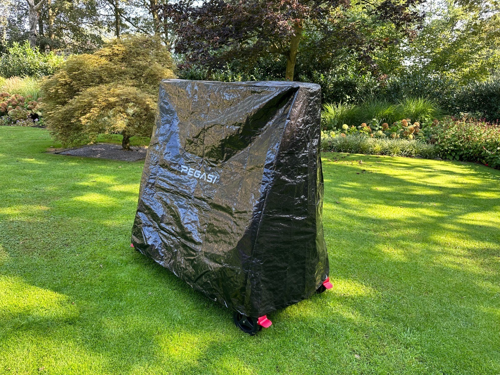 Black table tennis table covered with a black tarp in a grassy yard with trees.