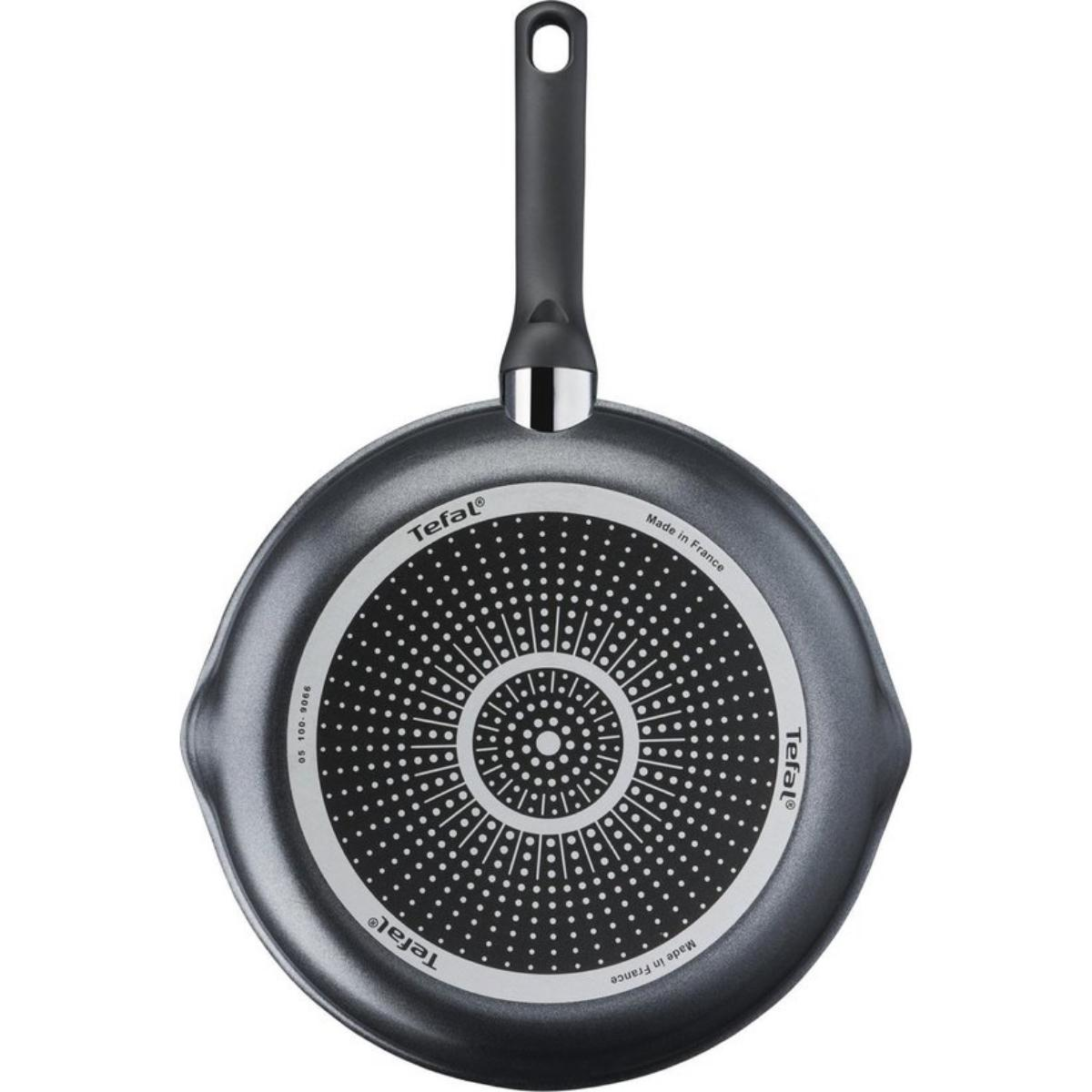 Spód szarej patelni Tefal z czarnym uchwytem. Podstawa ma okrągły wzór.