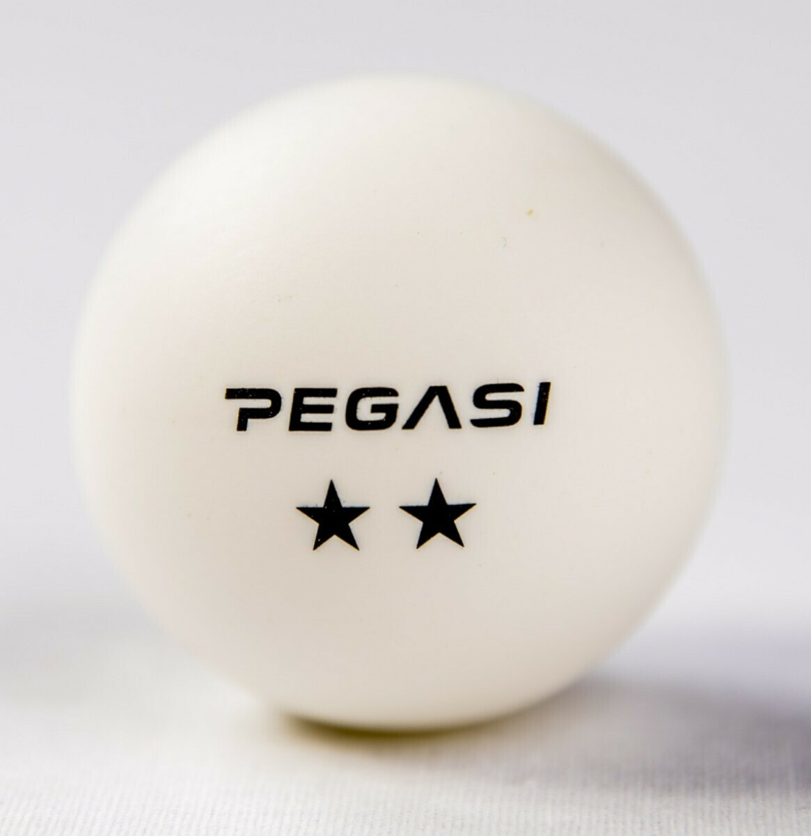 A white ping pong ball with the word 'PEGASI' and two stars printed on it.