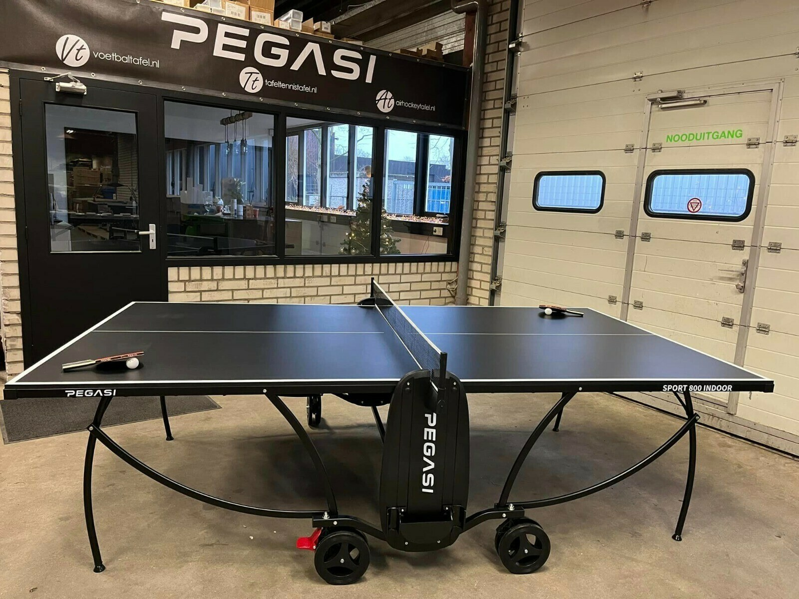 Black ping pong table with wheels, net, and a store background with a garage door.