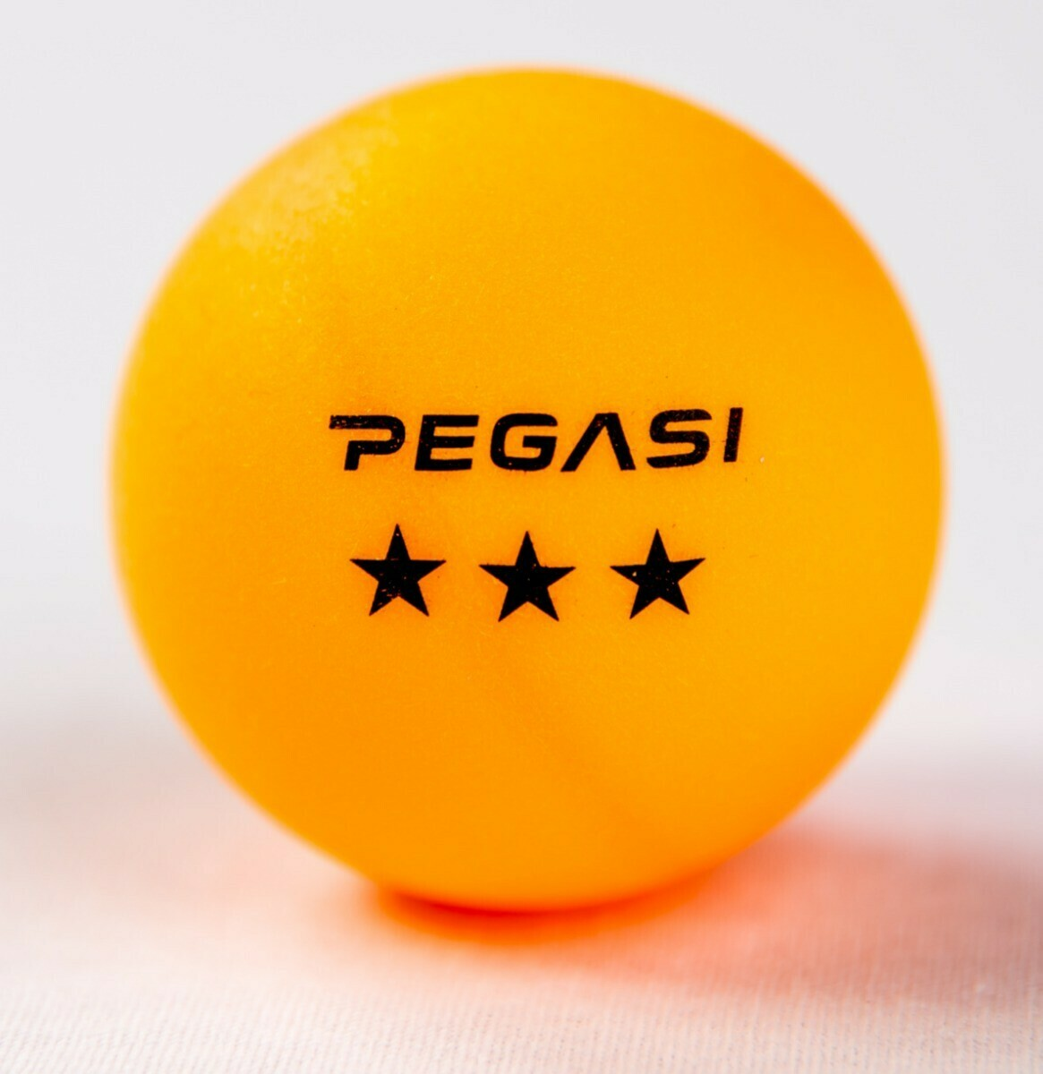 An orange ping pong ball with the brand name PEGASi and three stars printed on it.