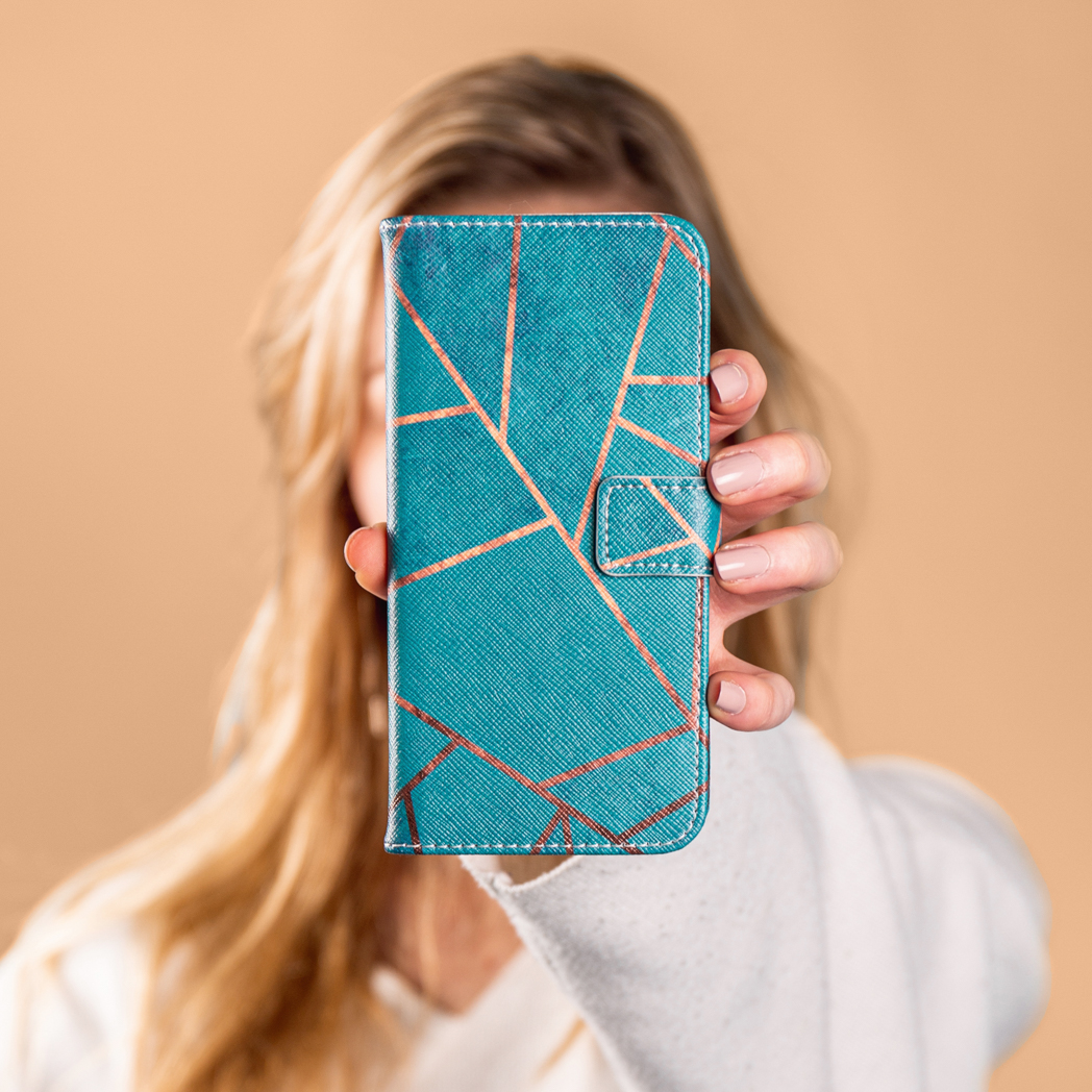 Femme tenant une coque de téléphone géométrique bleu sarcelle et cuivre. Fond beige.