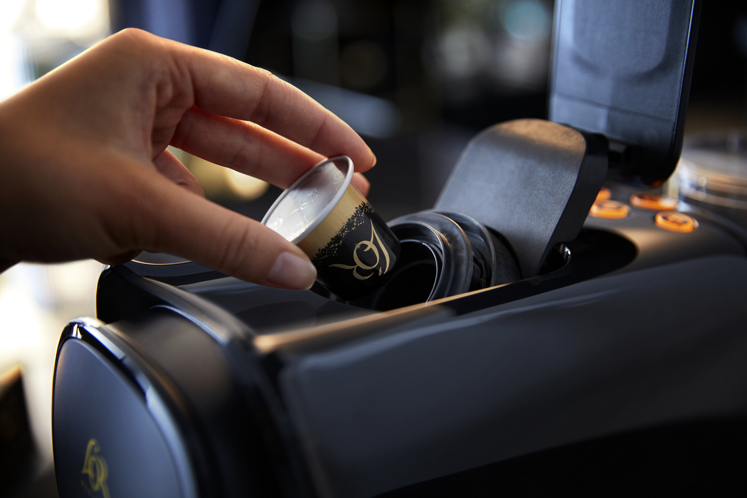 Ręka wkładająca kapsułkę z kawą do czarnego ekspresu do kawy.