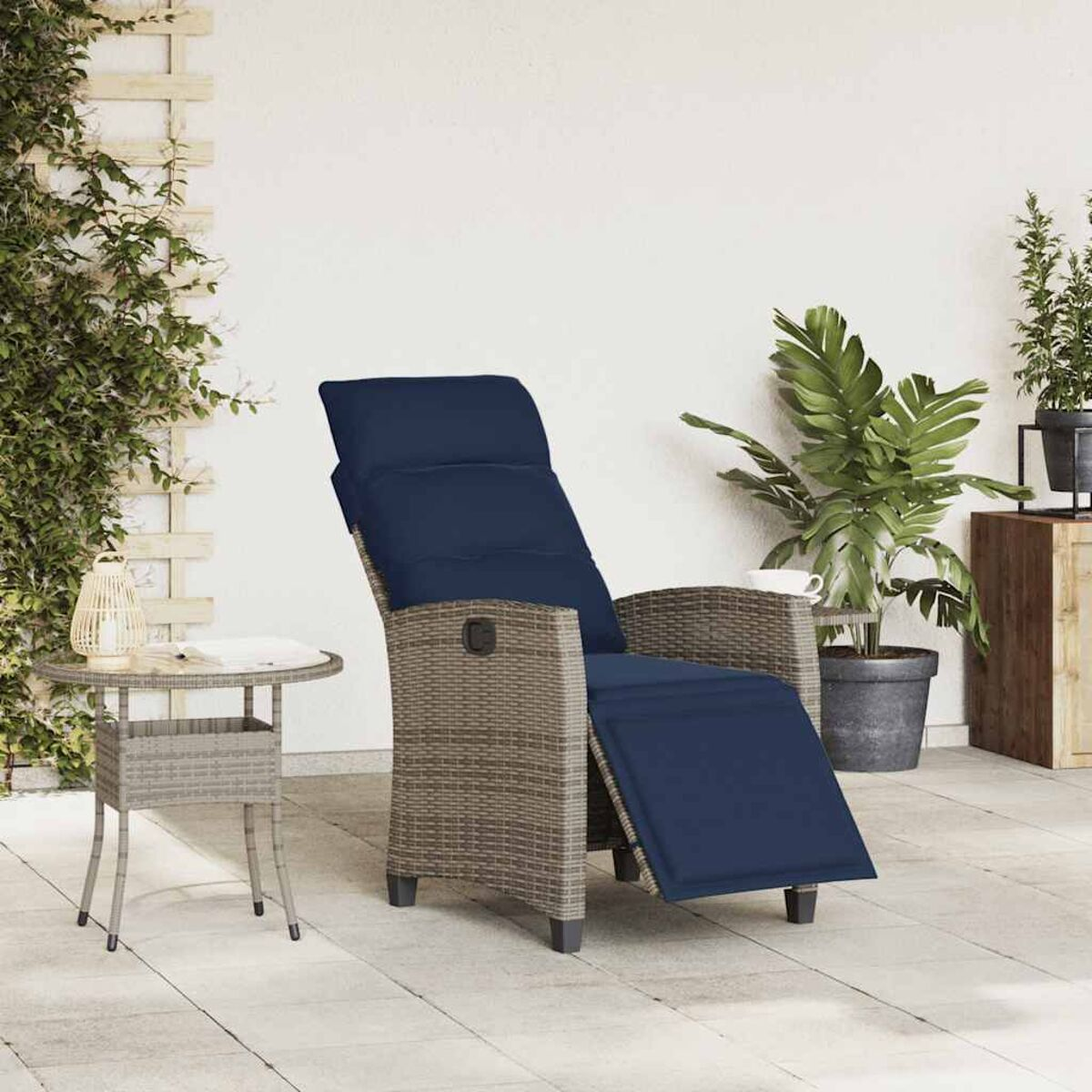 Scena all'aperto con una poltrona reclinabile in rattan con cuscino blu, un tavolino e piante.