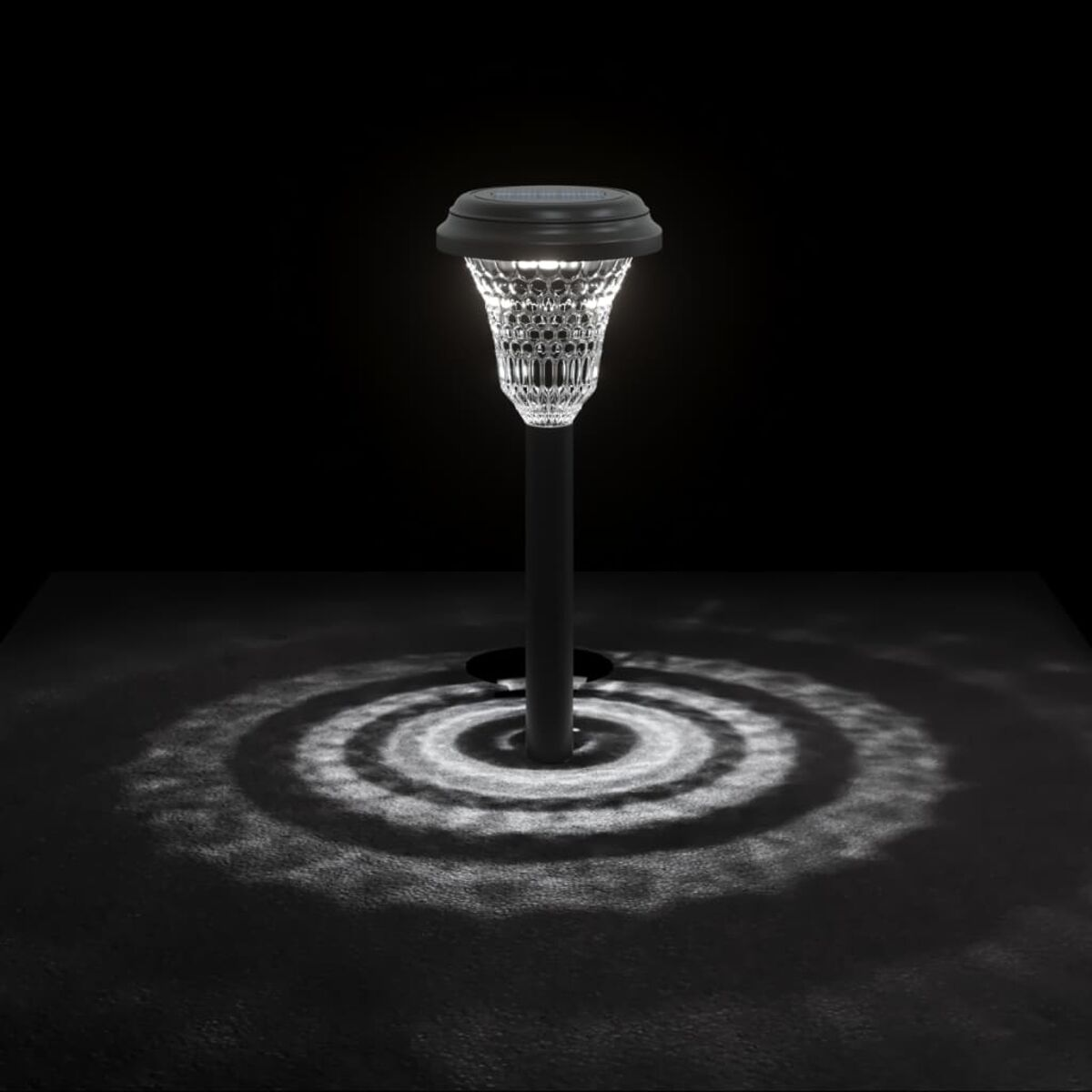 Una luce solare da giardino, che illumina una superficie scura, creando un motivo circolare.