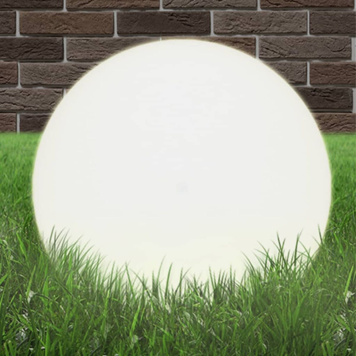 Sfera bianca brillante nell'erba verde, con un muro di mattoni sullo sfondo.