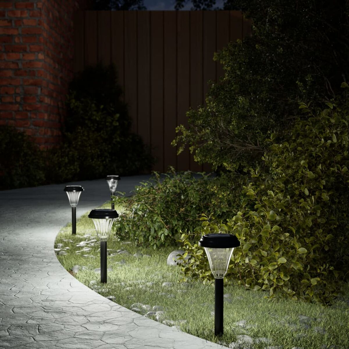 Sentiero con luci da giardino. Cespugli e una staccionata in legno sullo sfondo.