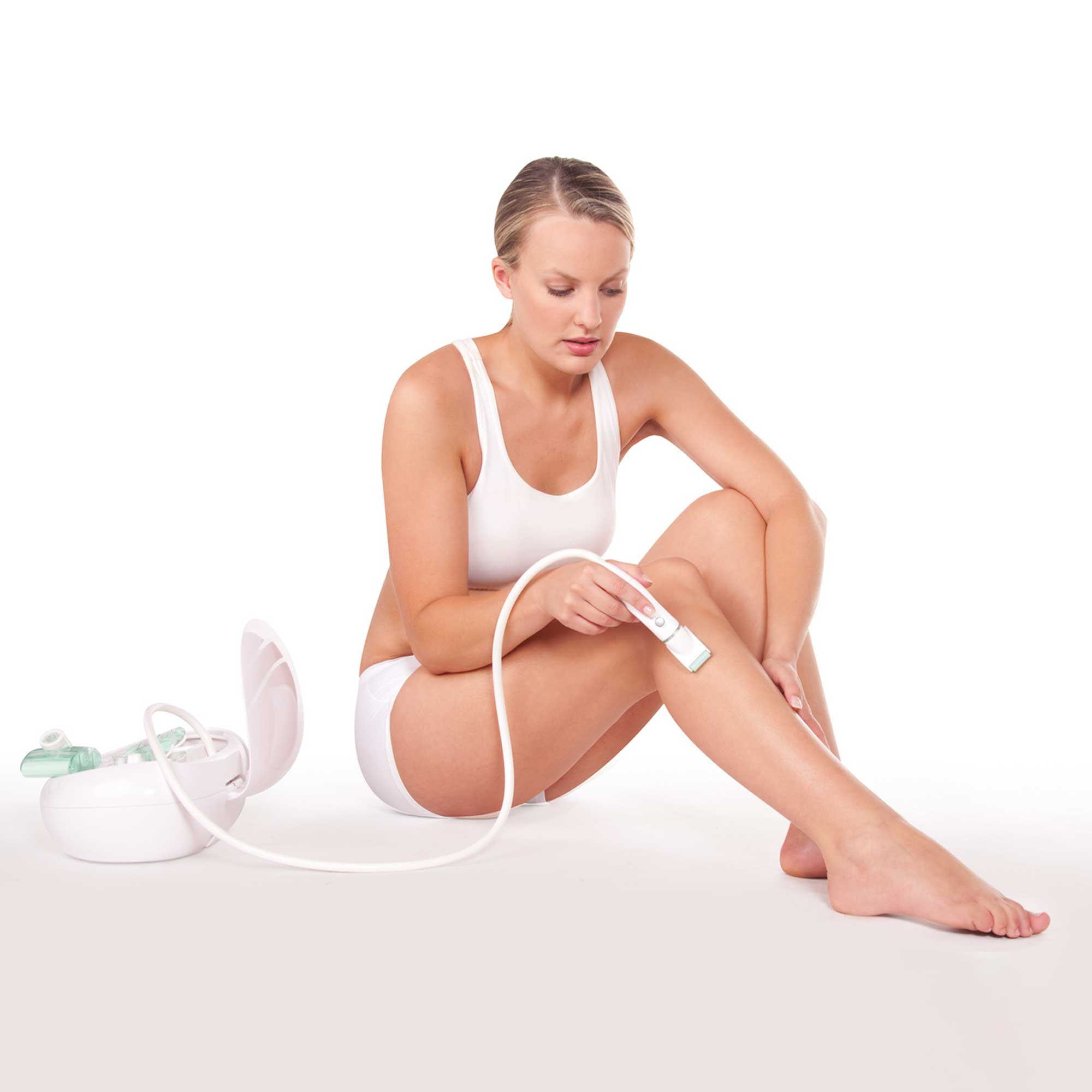 Woman sitting, using a hair removal device on her leg. White background and white accessories.