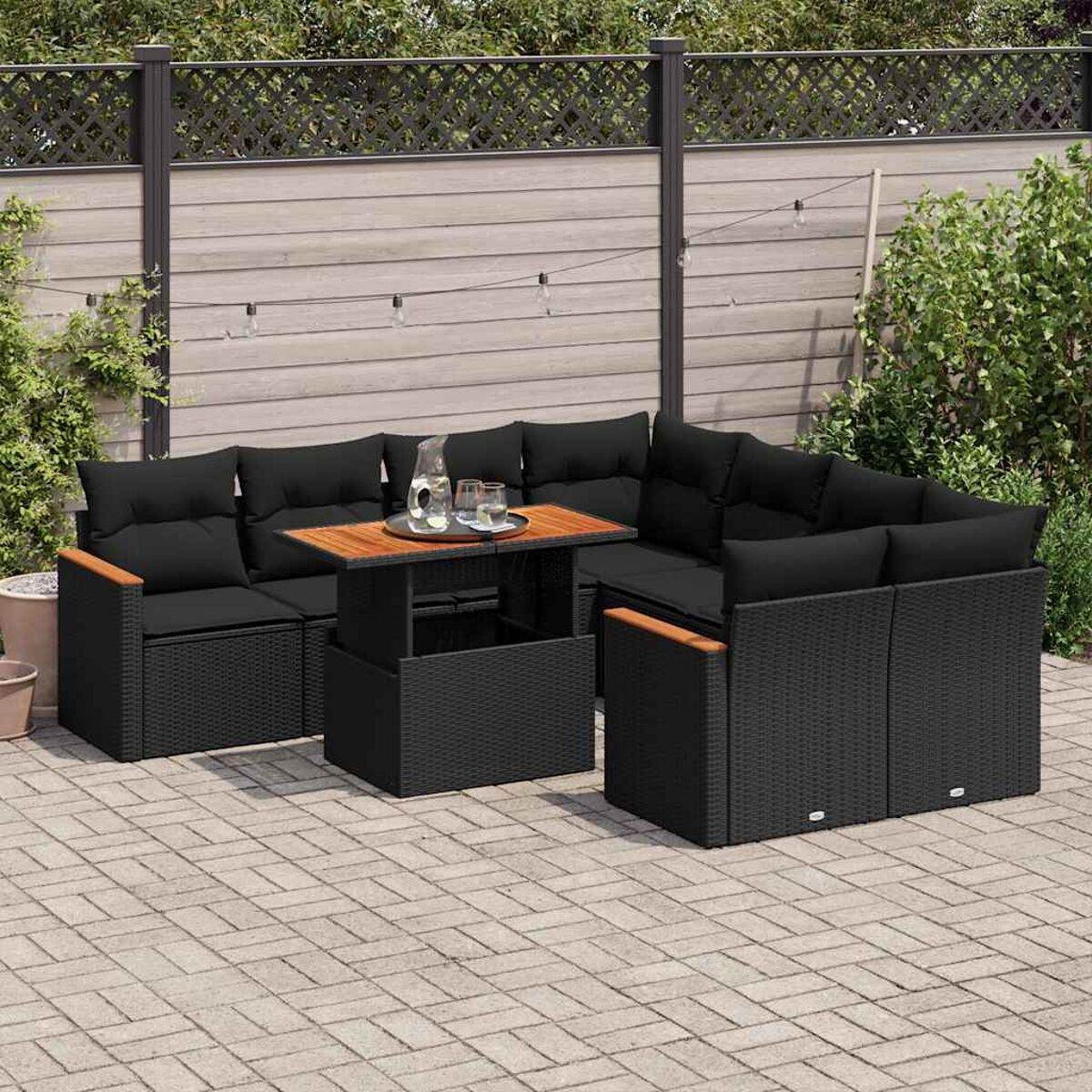Set divano in vimini nero da esterno con cuscini, tavolo in legno e giardino.