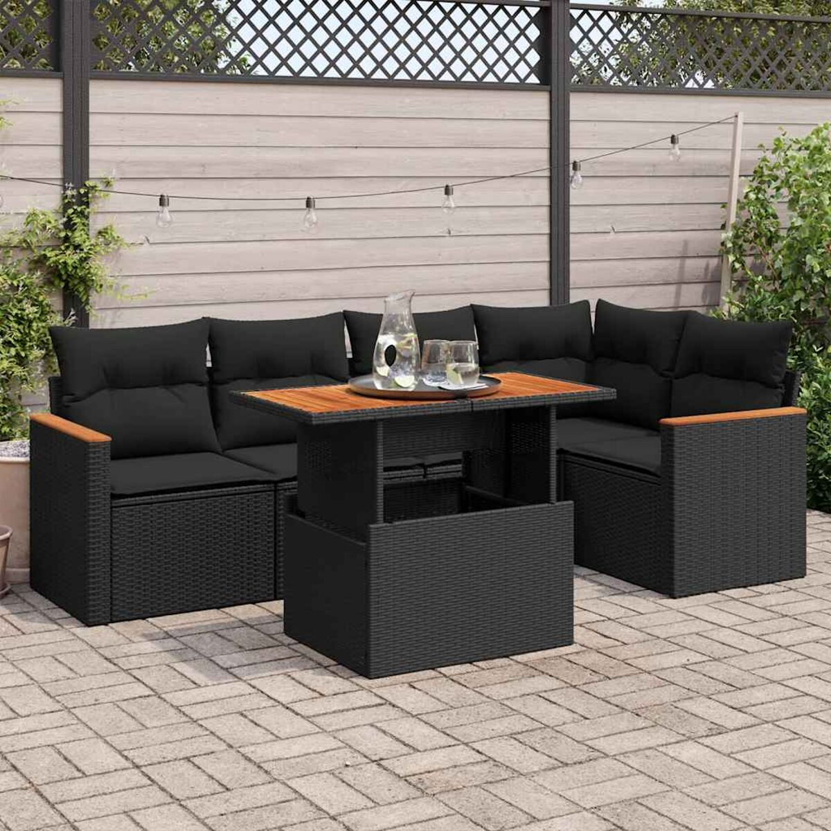 Set di mobili da esterno in rattan nero con cuscini, tavolo e piante.