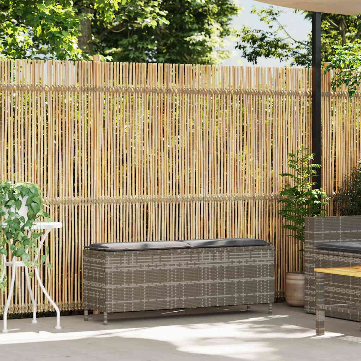 Recinzione in bambù con cassapanca grigia, mobili da giardino e piante.