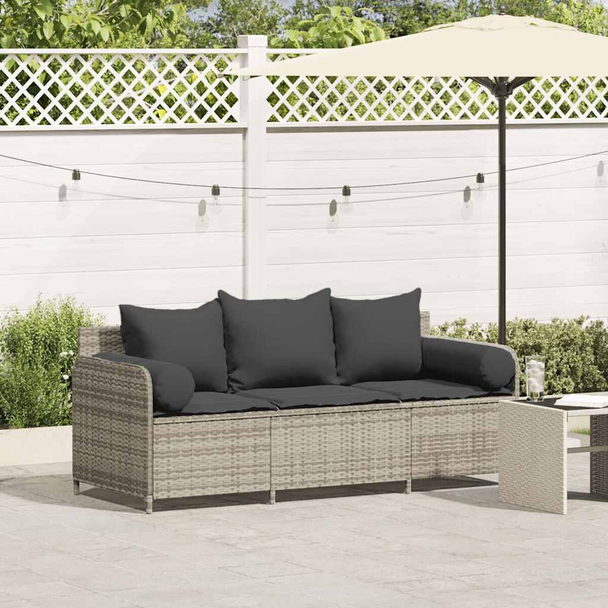 Un divano in rattan grigio con tre cuscini e un tavolino su un patio.
