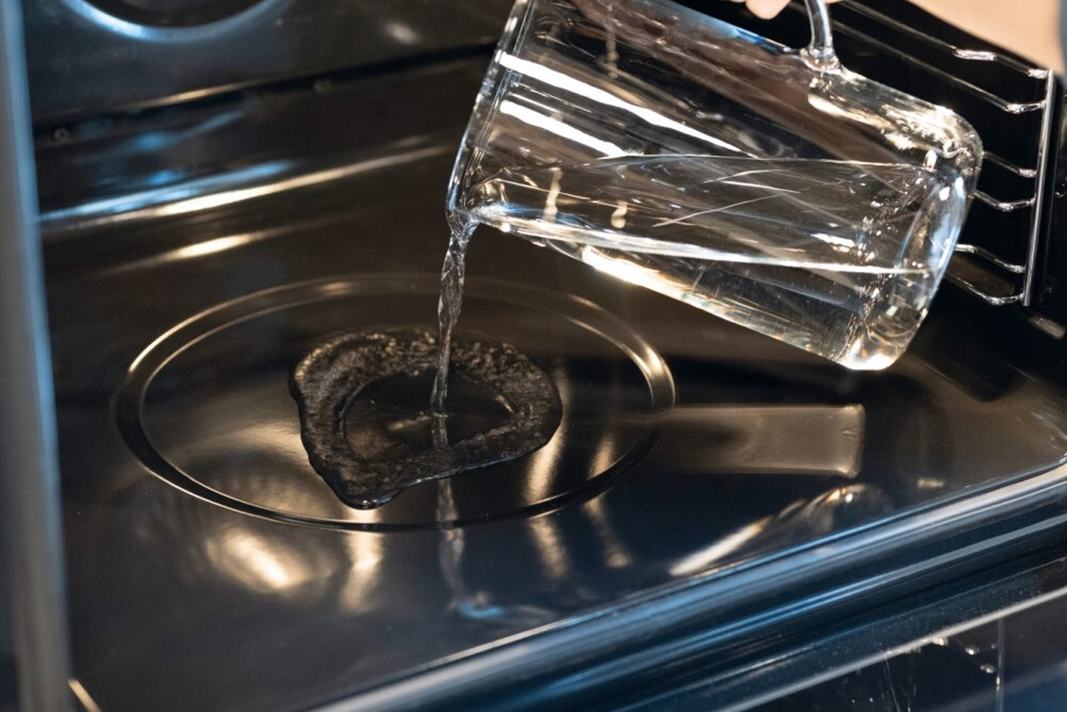Acqua versata da una brocca di vetro all'interno scuro di un forno.