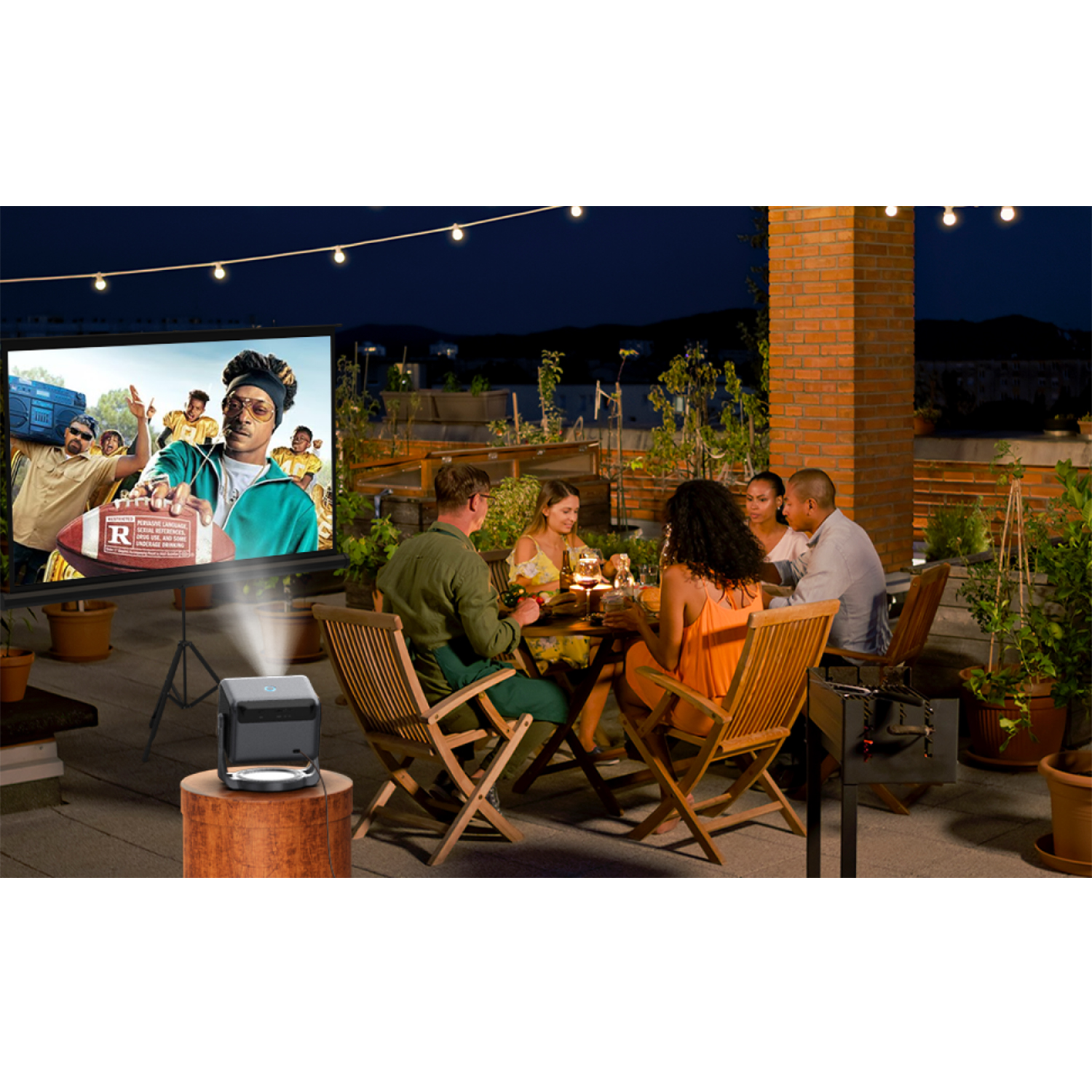 Ludzie oglądający film na ekranie. Projektor stoi na drewnianym stojaku na zewnątrz.