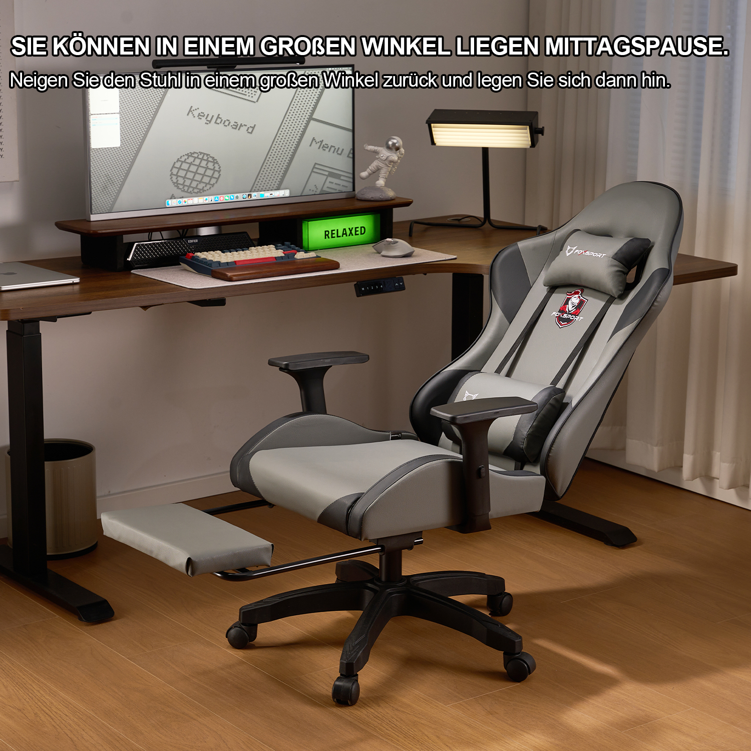 Grauer ergonomischer Stuhl mit Fußstütze in einem Raum mit Schreibtisch und Computer.