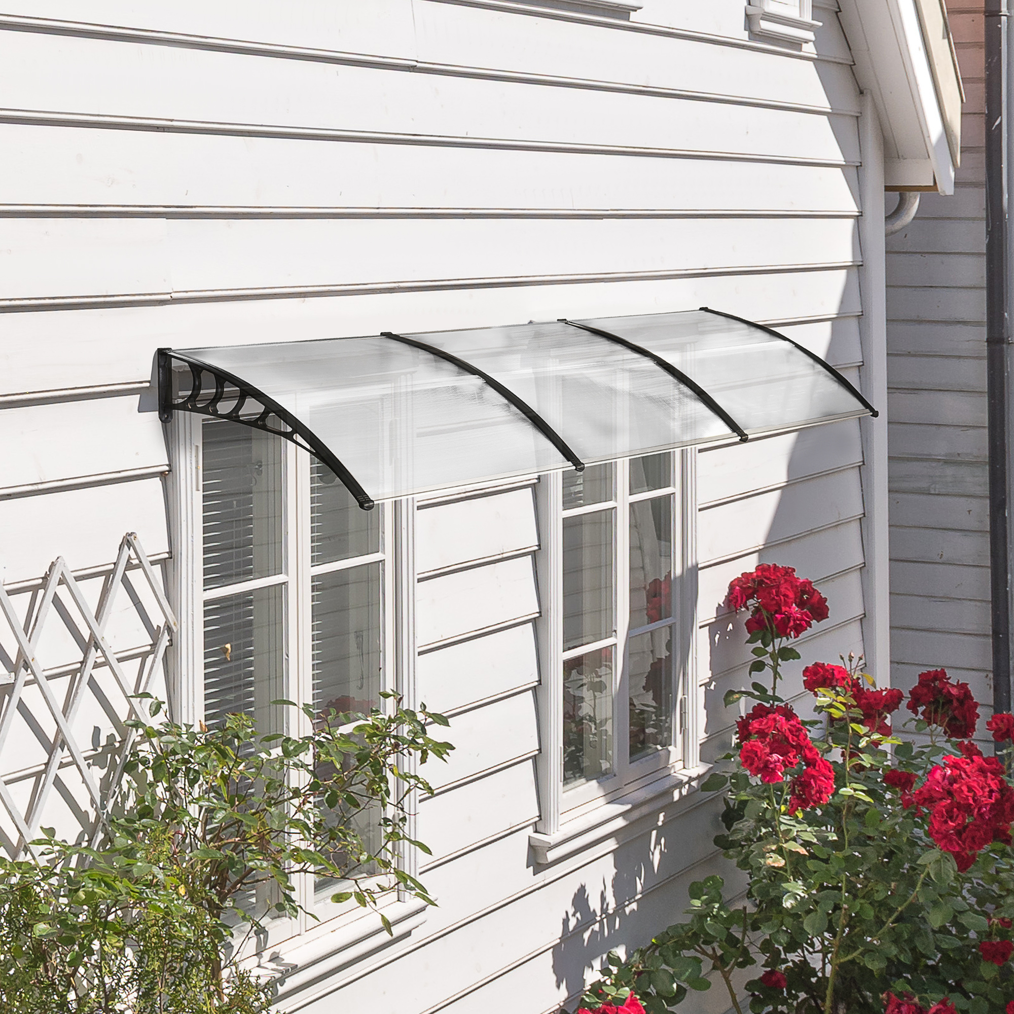 Weißes Haus mit Fenster-Markise. Eine schwarze Markise über zwei Fenstern, rote Rosen rechts.