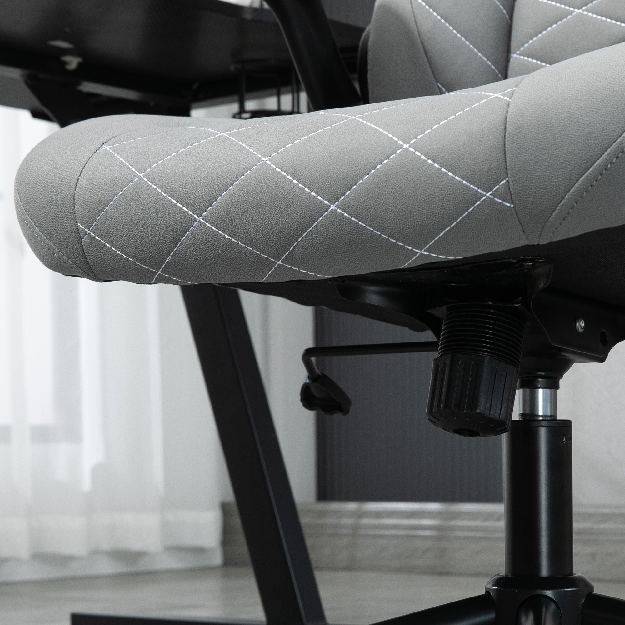 Nahaufnahme eines grauen Gaming-Stuhls mit weißen Steppdetails und schwarzem Fuß.
