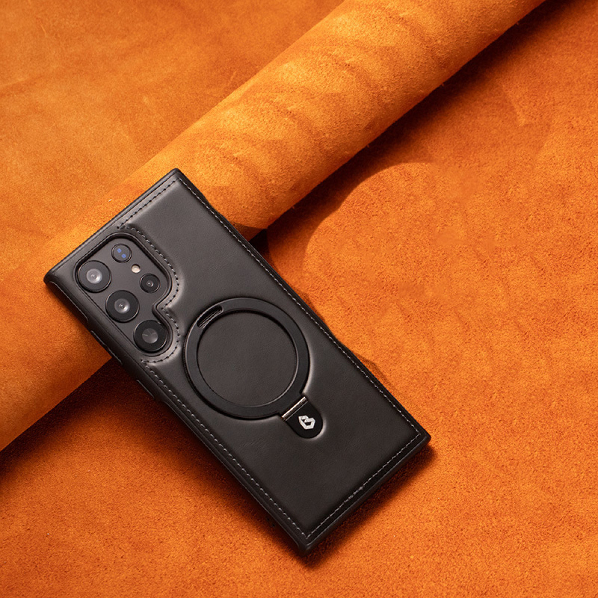 Custodia per telefono nera con un anello circolare su una texture di pelle arancione.