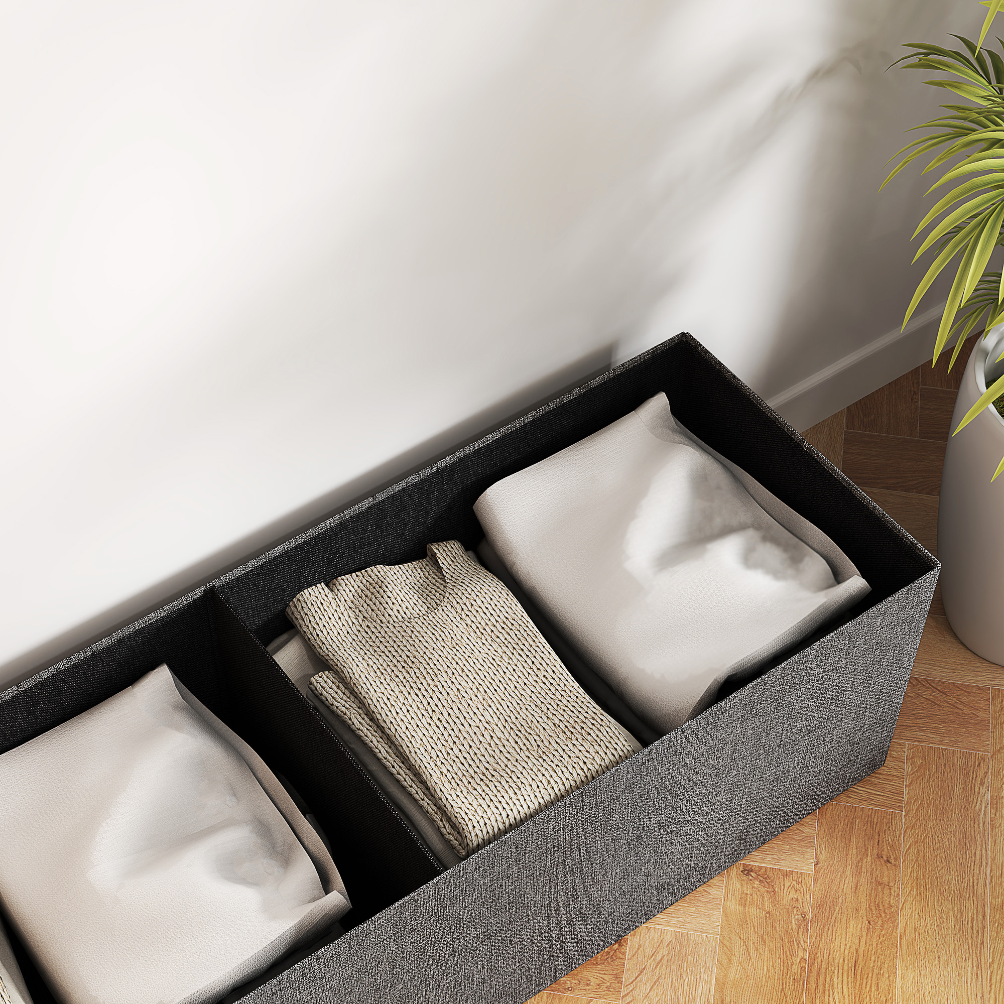 Eine graue Stoff-Aufbewahrungsbox mit drei Abschnitten, gefüllt mit gefalteter Kleidung. Der Hintergrund ist weiß.