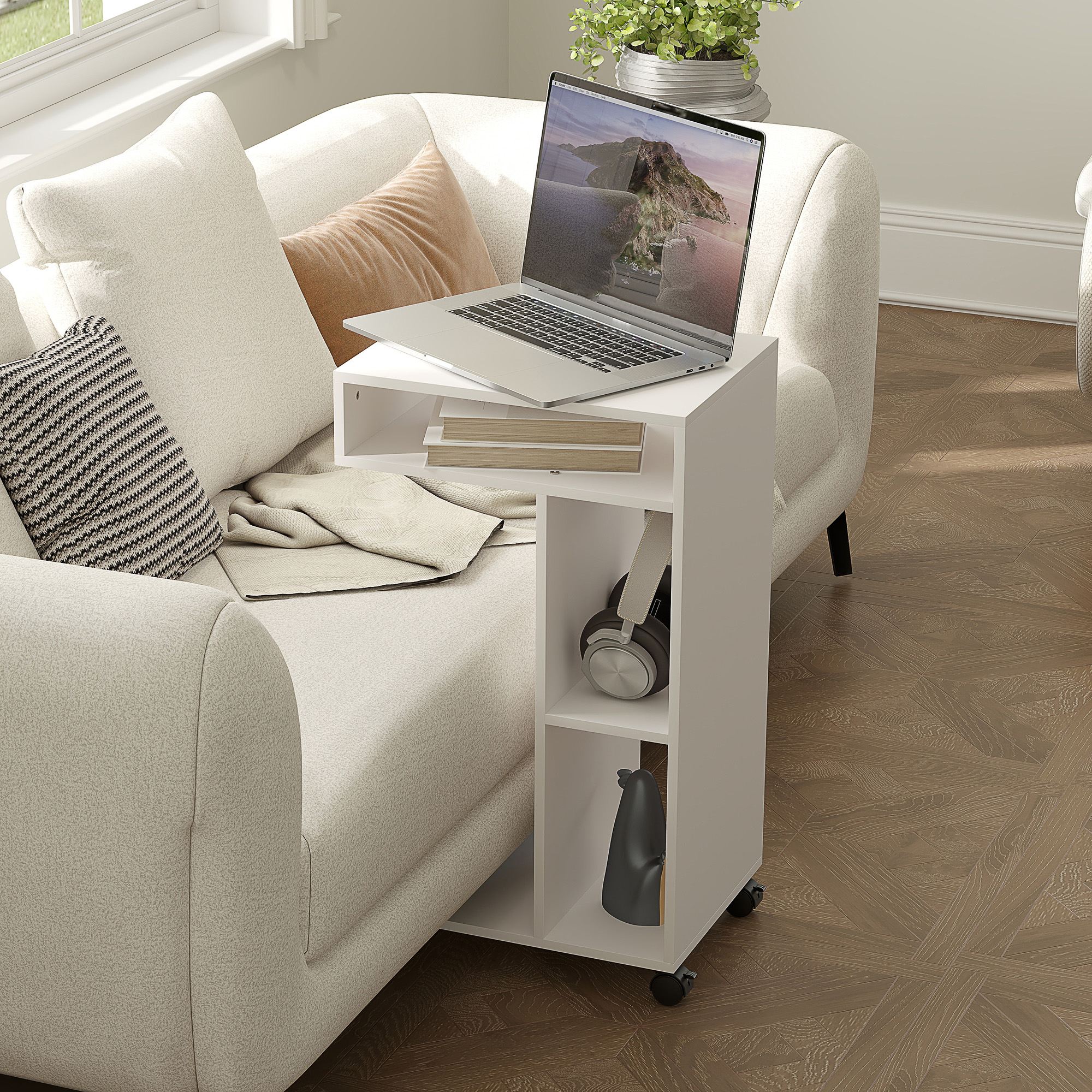 Weißer mobiler Beistelltisch mit Regalen und einem Laptop. Sofa und Kopfhörer im Hintergrund.
