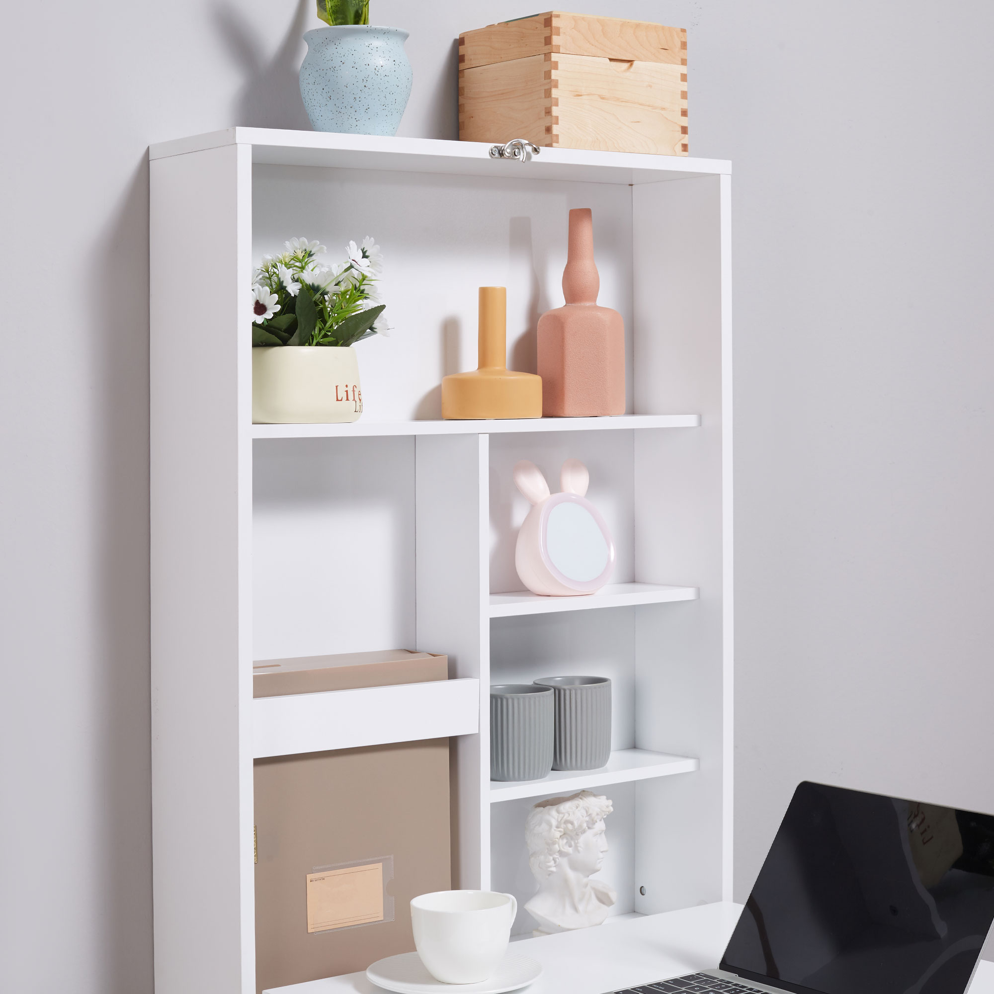 Ein weißer, an der Wand befestigter Schrank mit Regalen, Dekor und einem Laptop auf einem Schreibtisch.