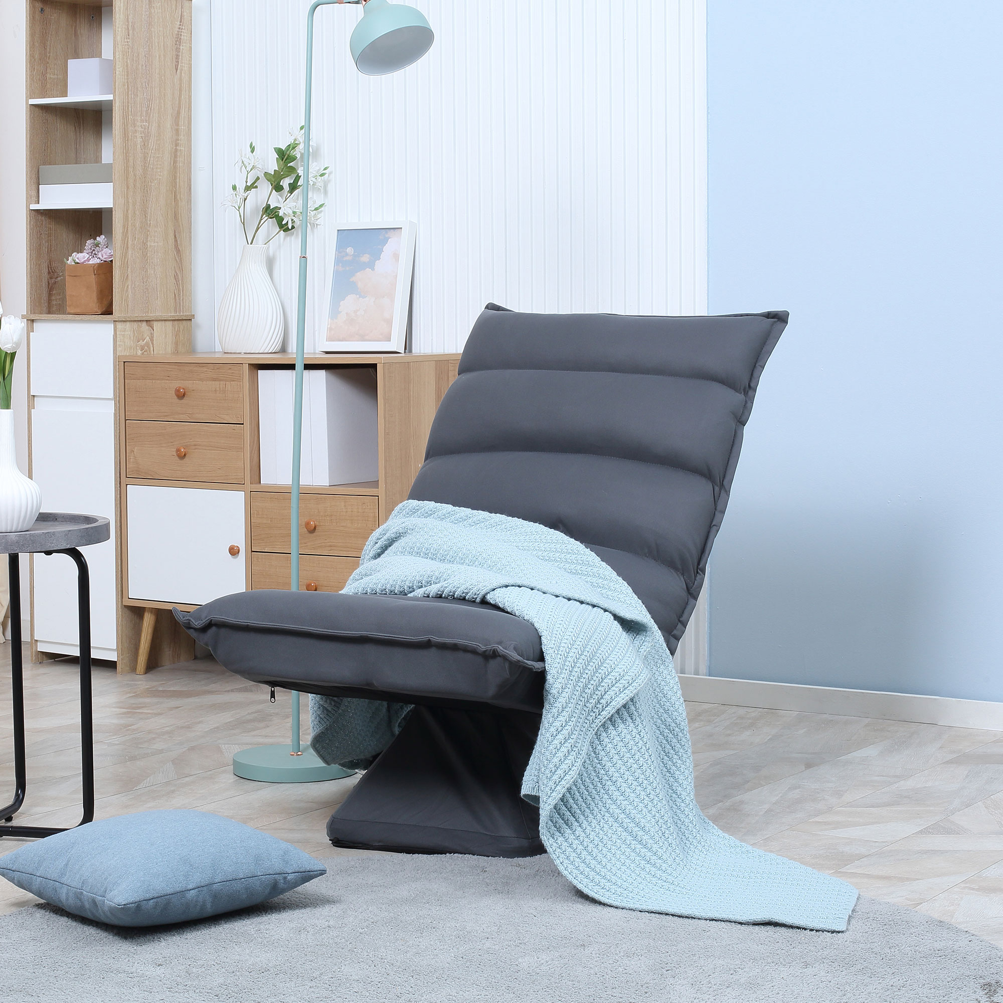 Eine Wohnzimmerszene mit einem grauen Relaxsessel, einer hellblauen Decke und einer Stehlampe.