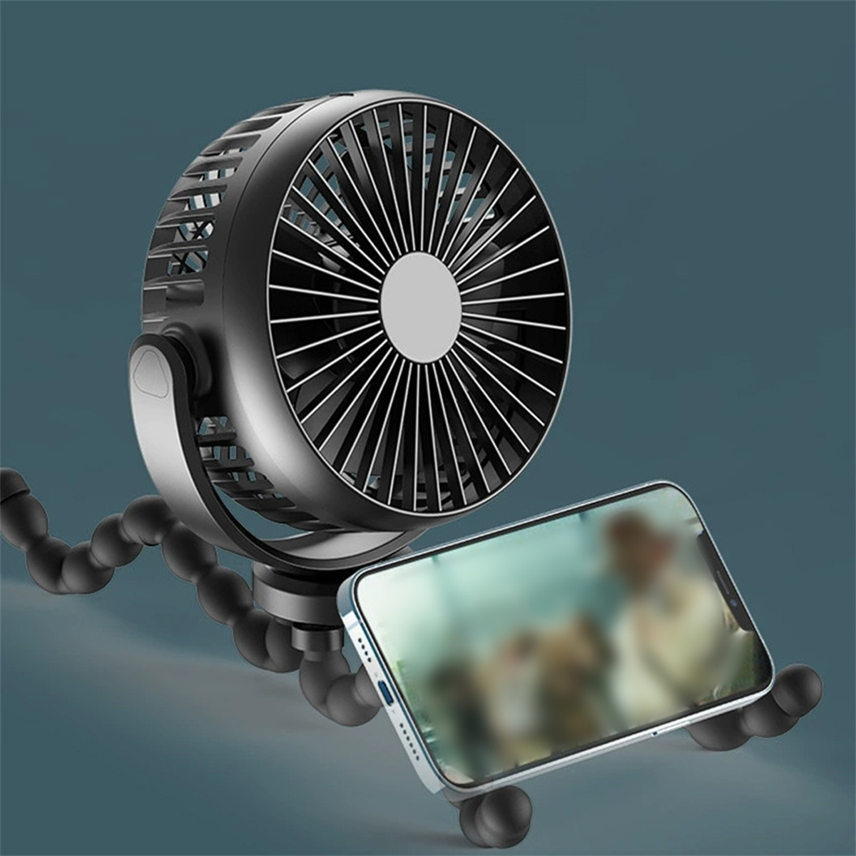 Ein schwarzer und silberner Ventilator auf einem flexiblen Stativ, neben einem Telefon mit verschwommenem Video.