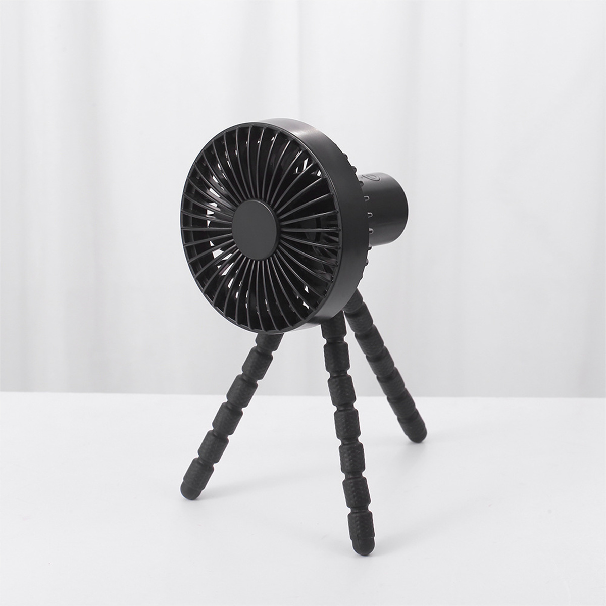 Ein schwarzer Stativventilator auf einer weißen Oberfläche. Der Ventilator hat flexible Beine.