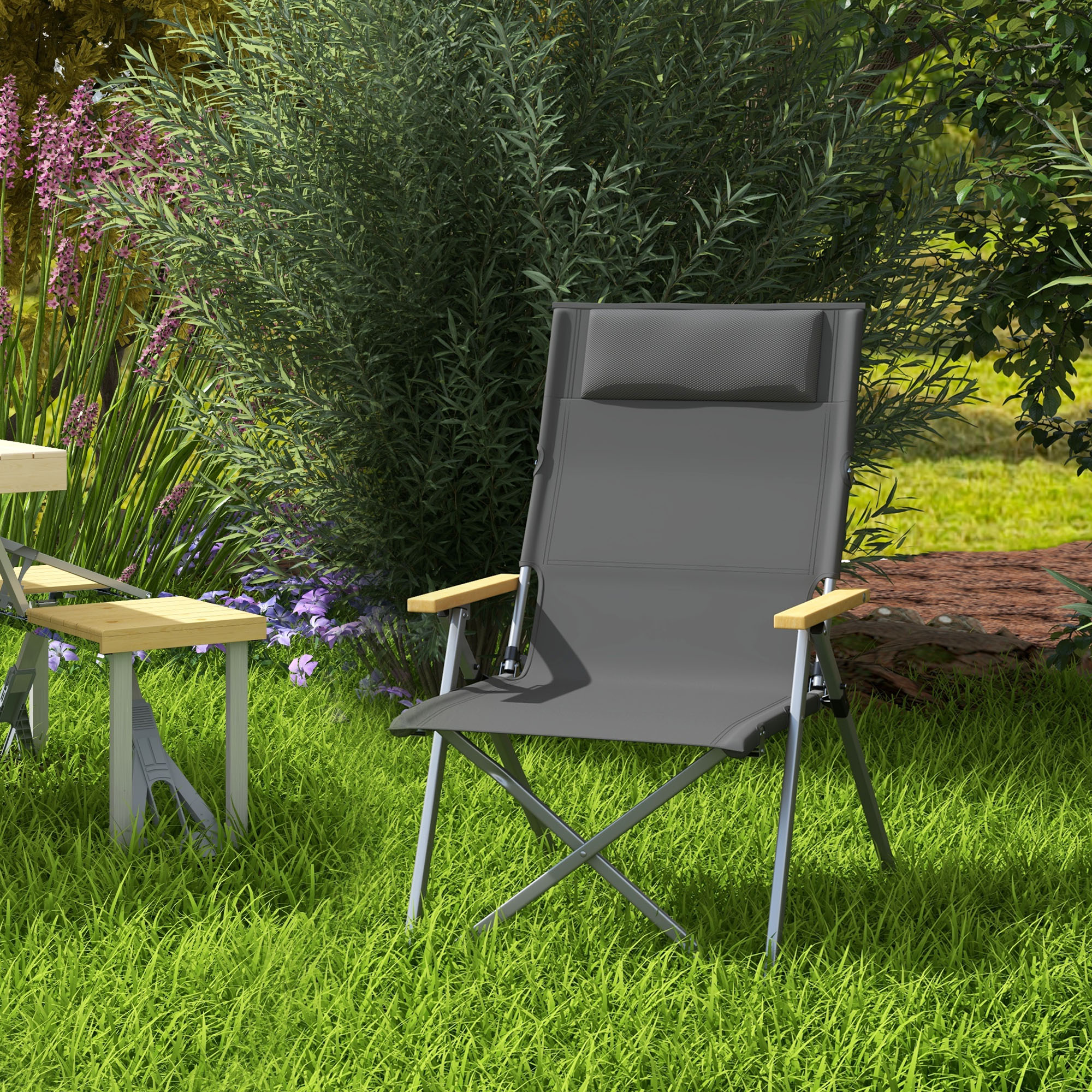 Grauer Campingstuhl mit Holzarmlehnen auf grünem Gras. Ein kleiner Tisch und ein Busch im Hintergrund.