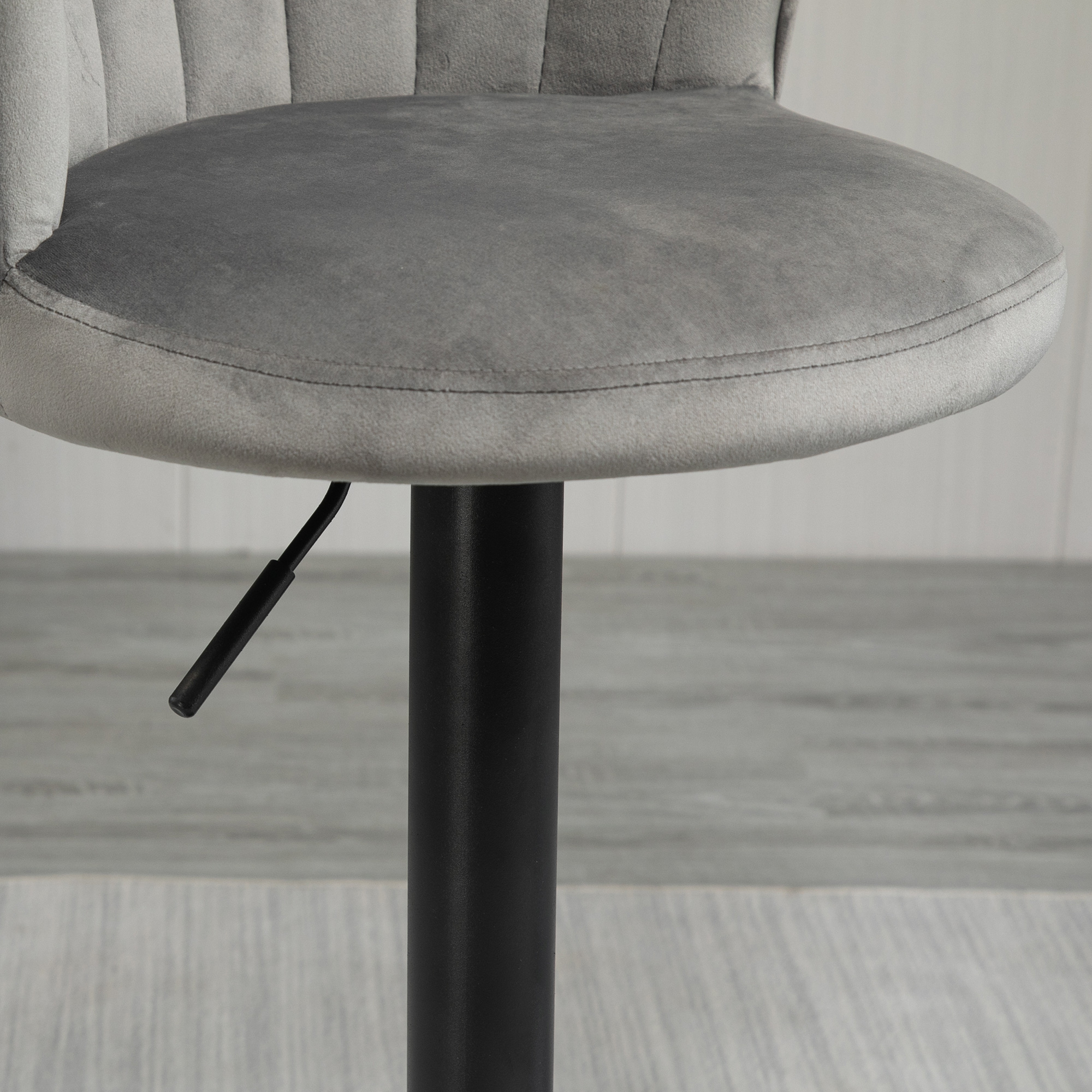 Grauer Barhocker mit einem Sitzpolster und schwarzem Stützfuß. Der Hintergrund ist ein Holzboden.
